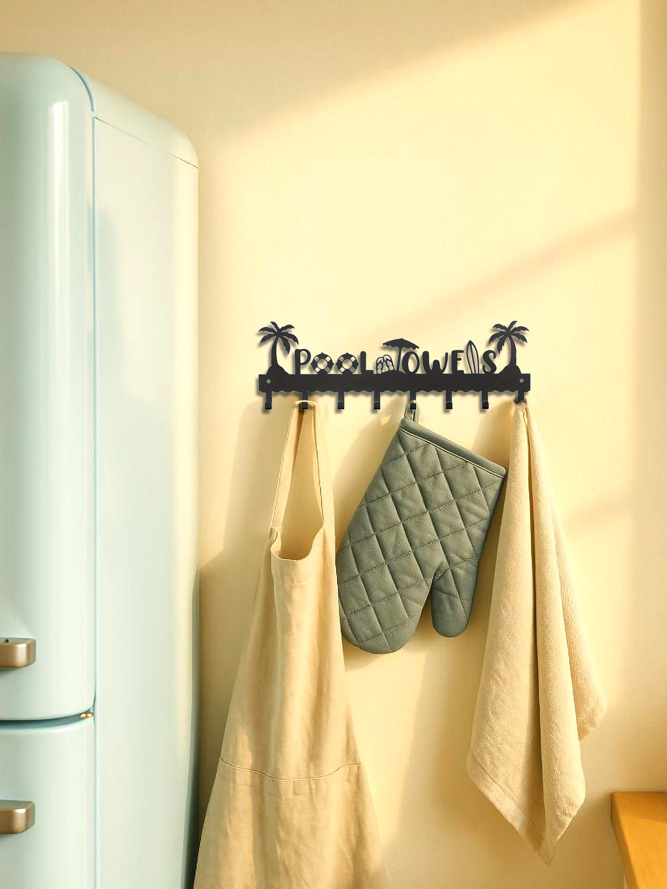 Beach themed wall-mounted hook with apron, oven mitts, and towel against a light-colored wall.