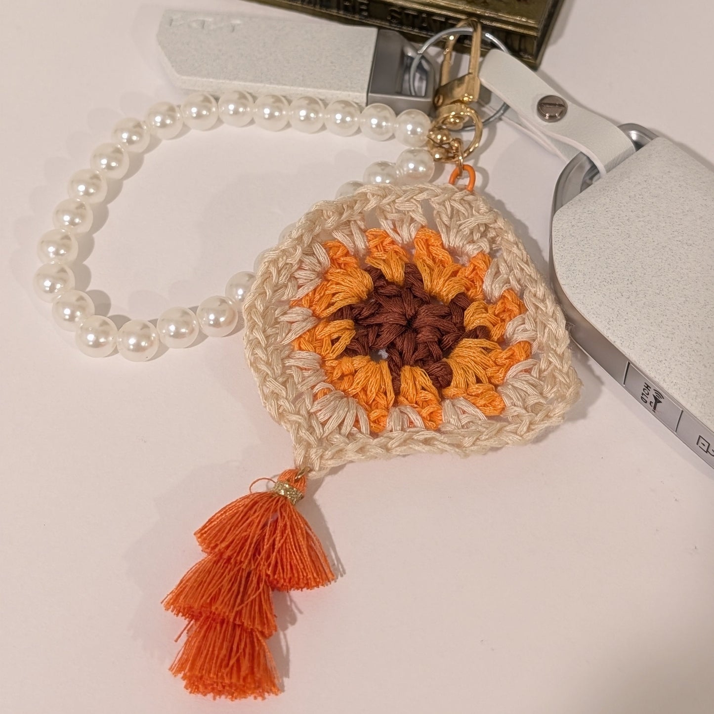 Beige crocheted keychain with orange and brown design, and orange tassel on a white surface