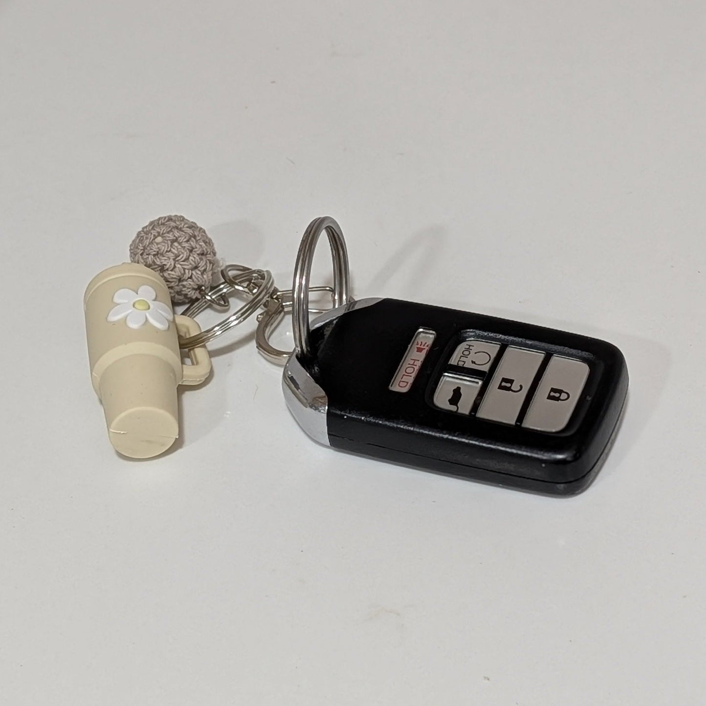 Beige little silicone tumbler key chain with crochet ball placed on a white kitchen countertop
