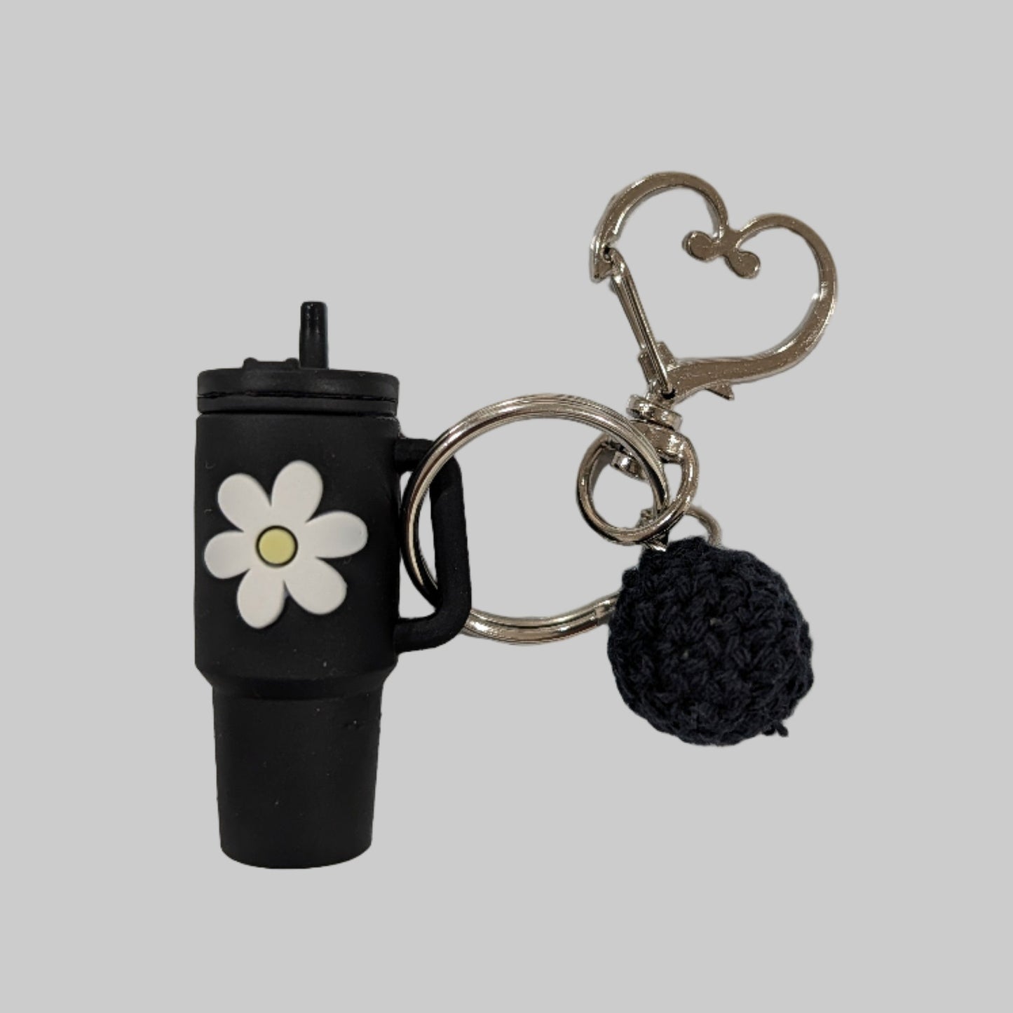 Black little silicone tumbler keychain with a flower charm and heart-shaped clip on a white background