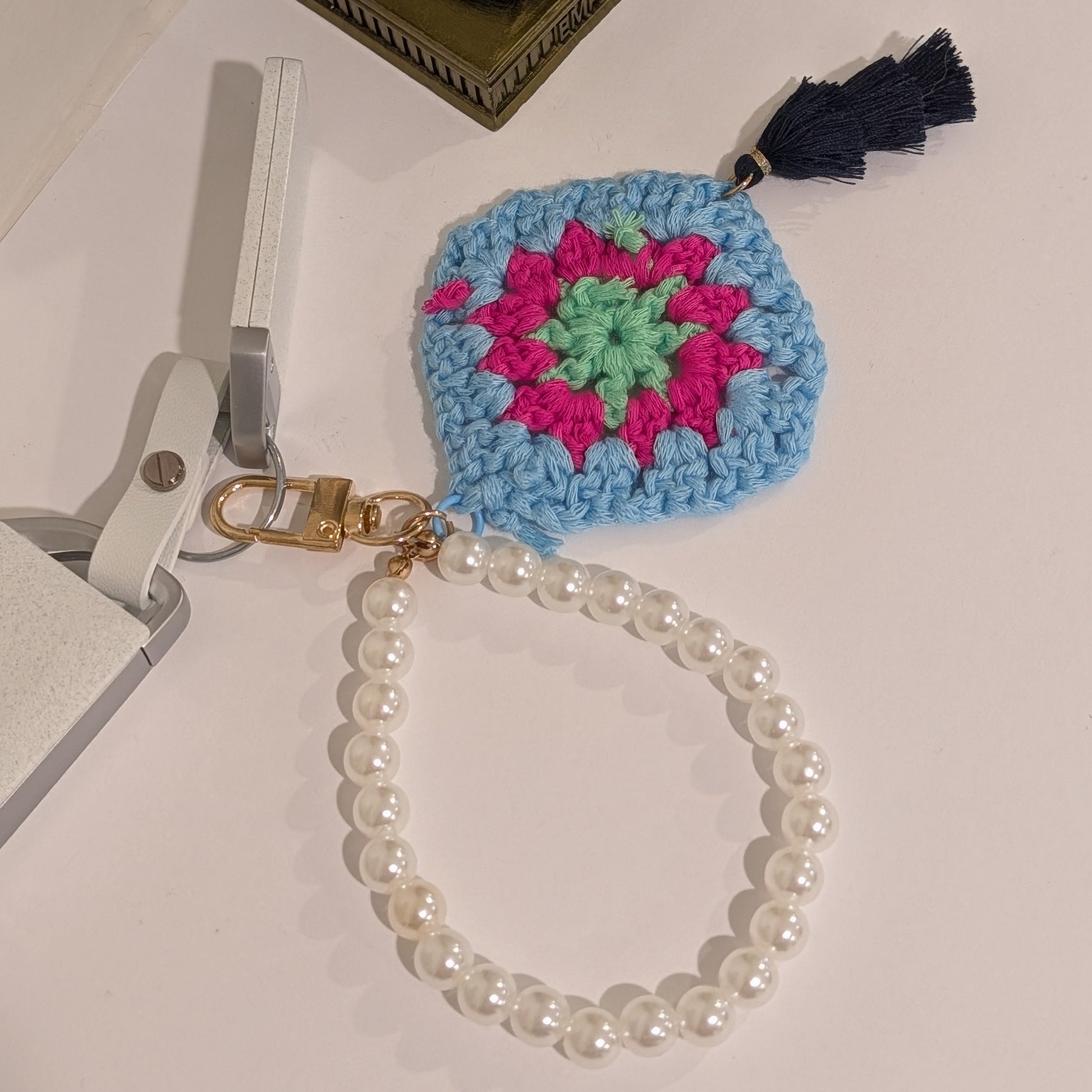 Blue Crocheted keychain with colorful design and black tassel on a white surface.