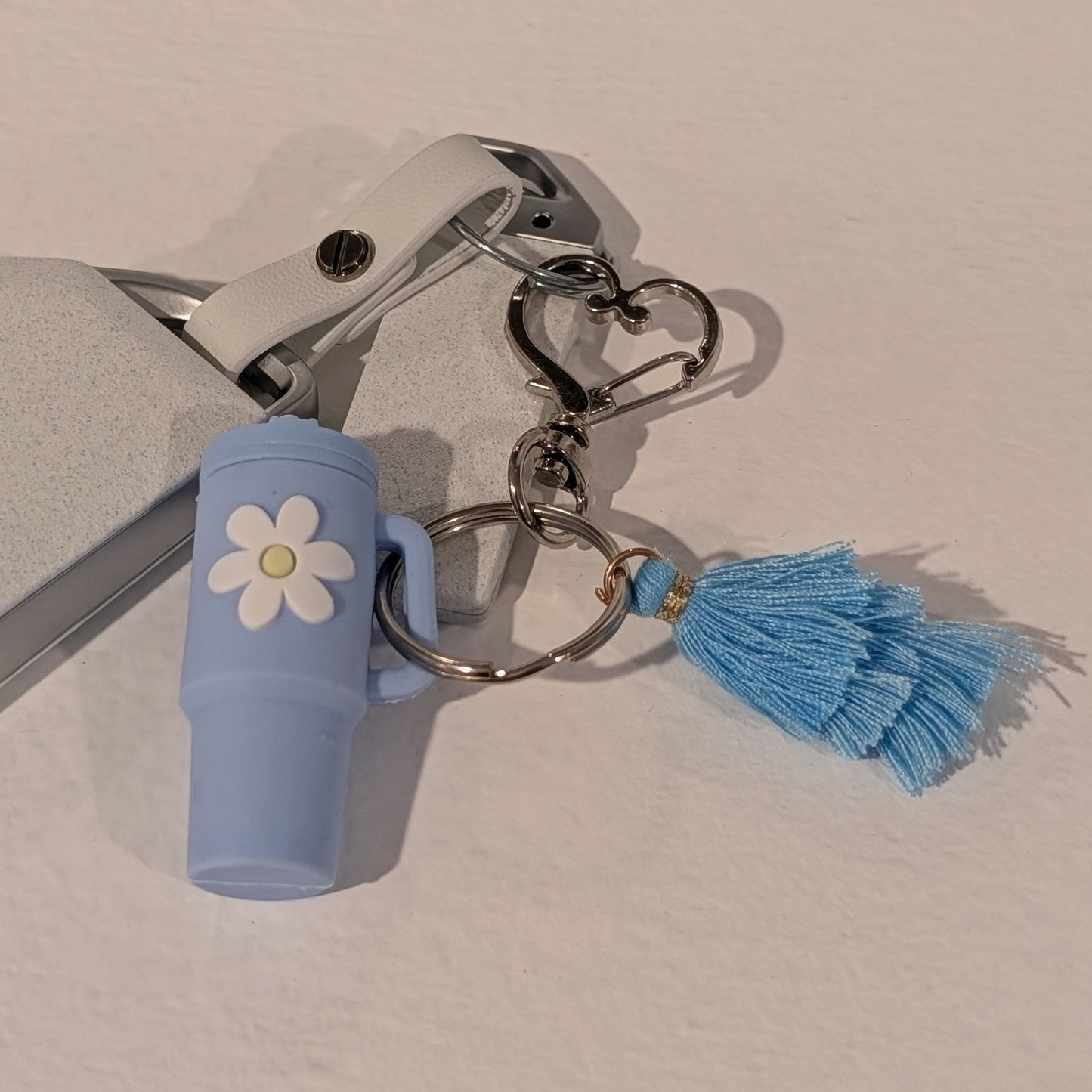 Blue keychain with a flower charm, heart shaped hook and tassel on a light background