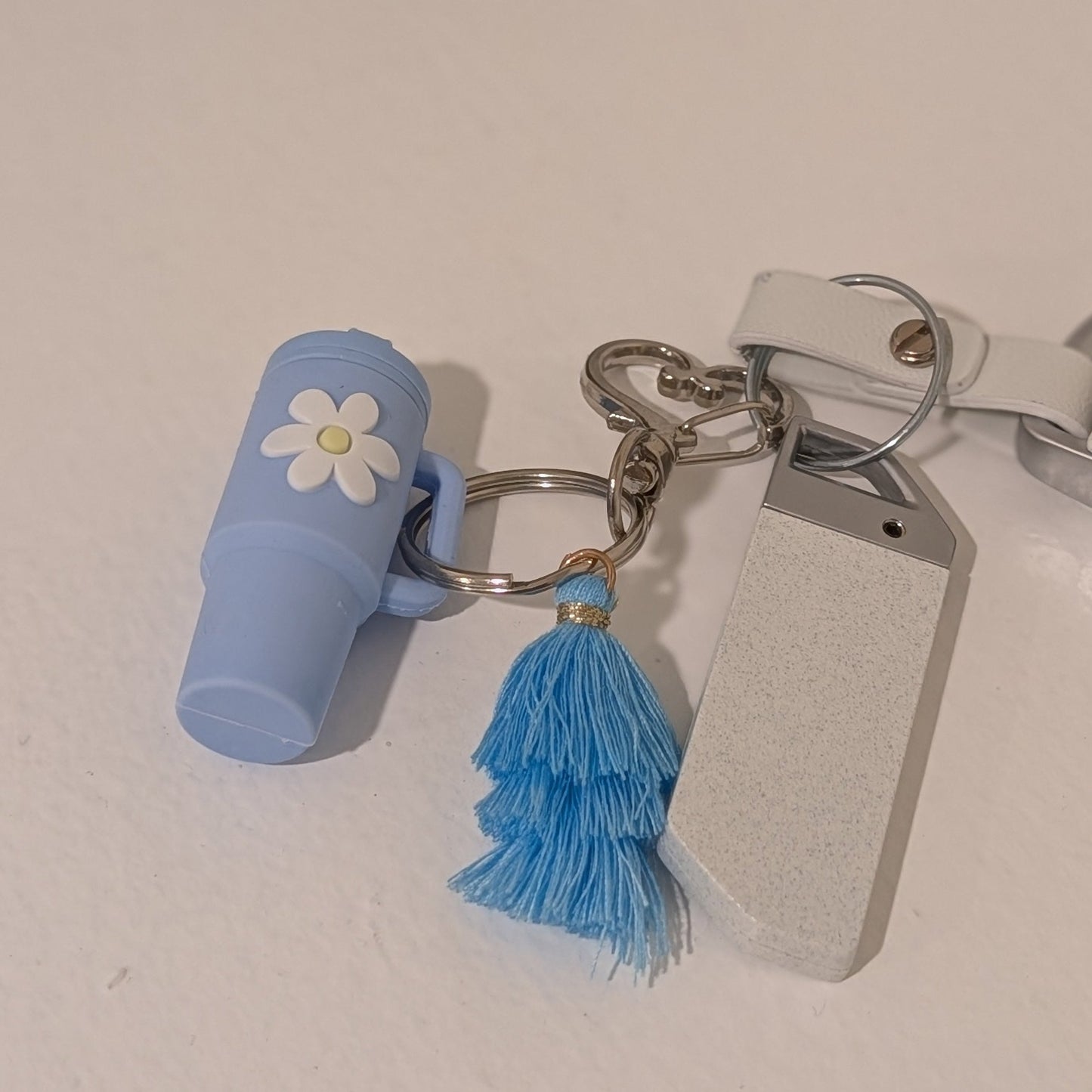 Blue keychain with a flower charm, heart shaped hook and tassel on a light background