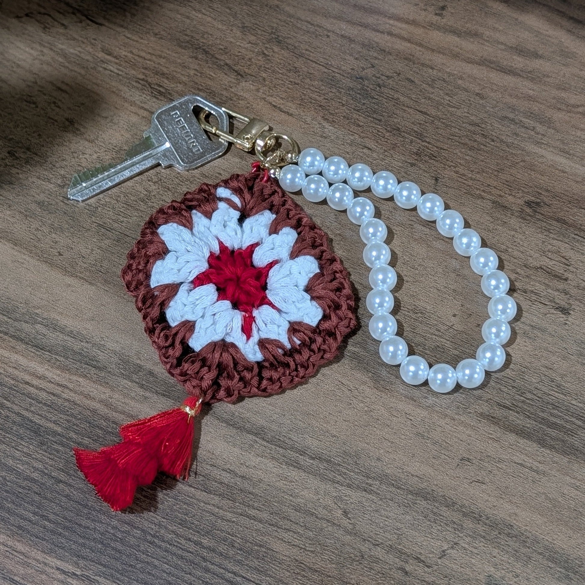 Crocheted keychain with a red and white flower design on a wooden surface