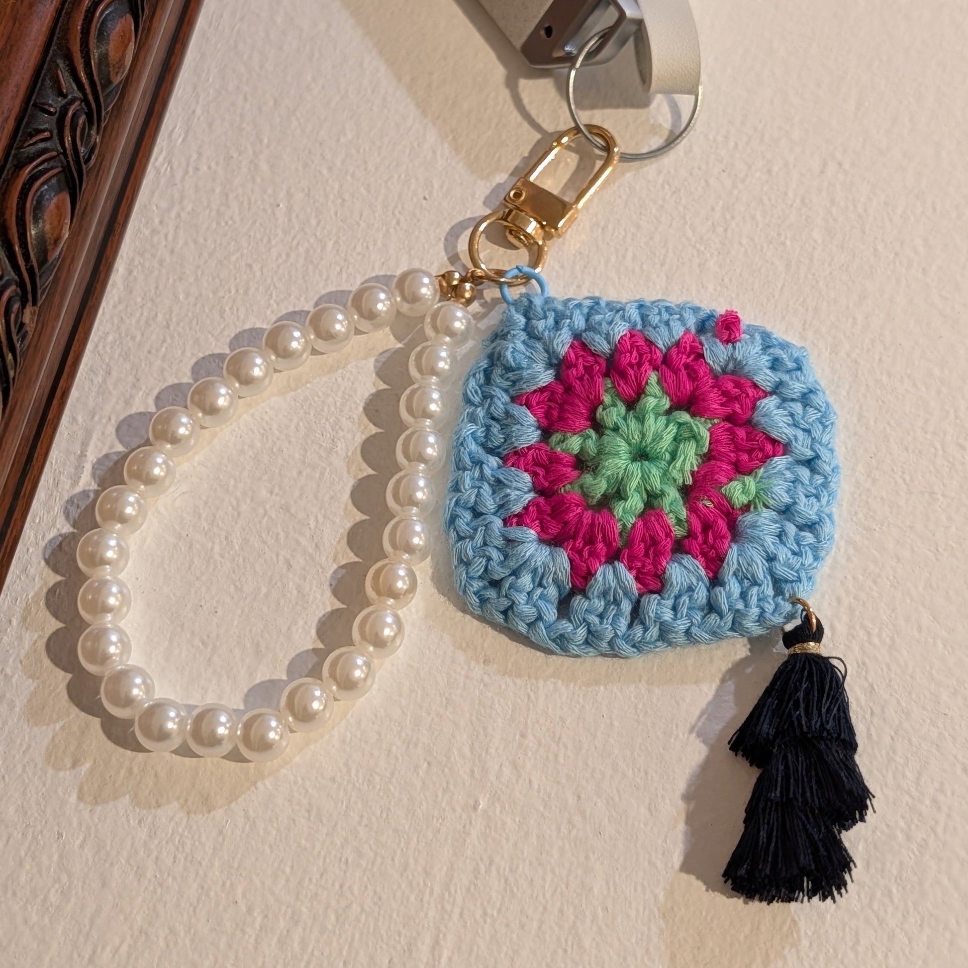 Crocheted keychain with colorful design and black tassel on a light surface