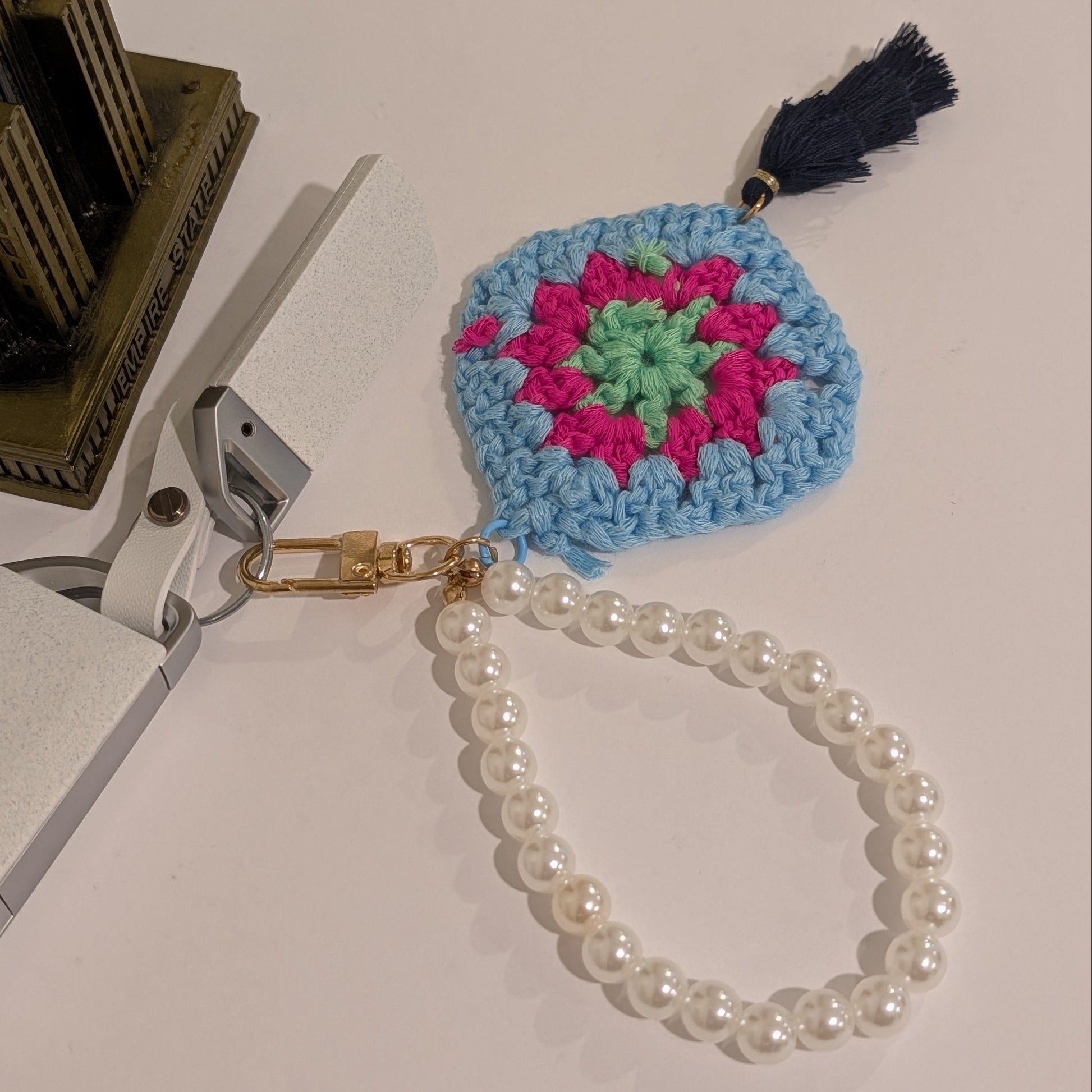 Crocheted keychain with colorful design, black tassel and white pearl chain on a white background