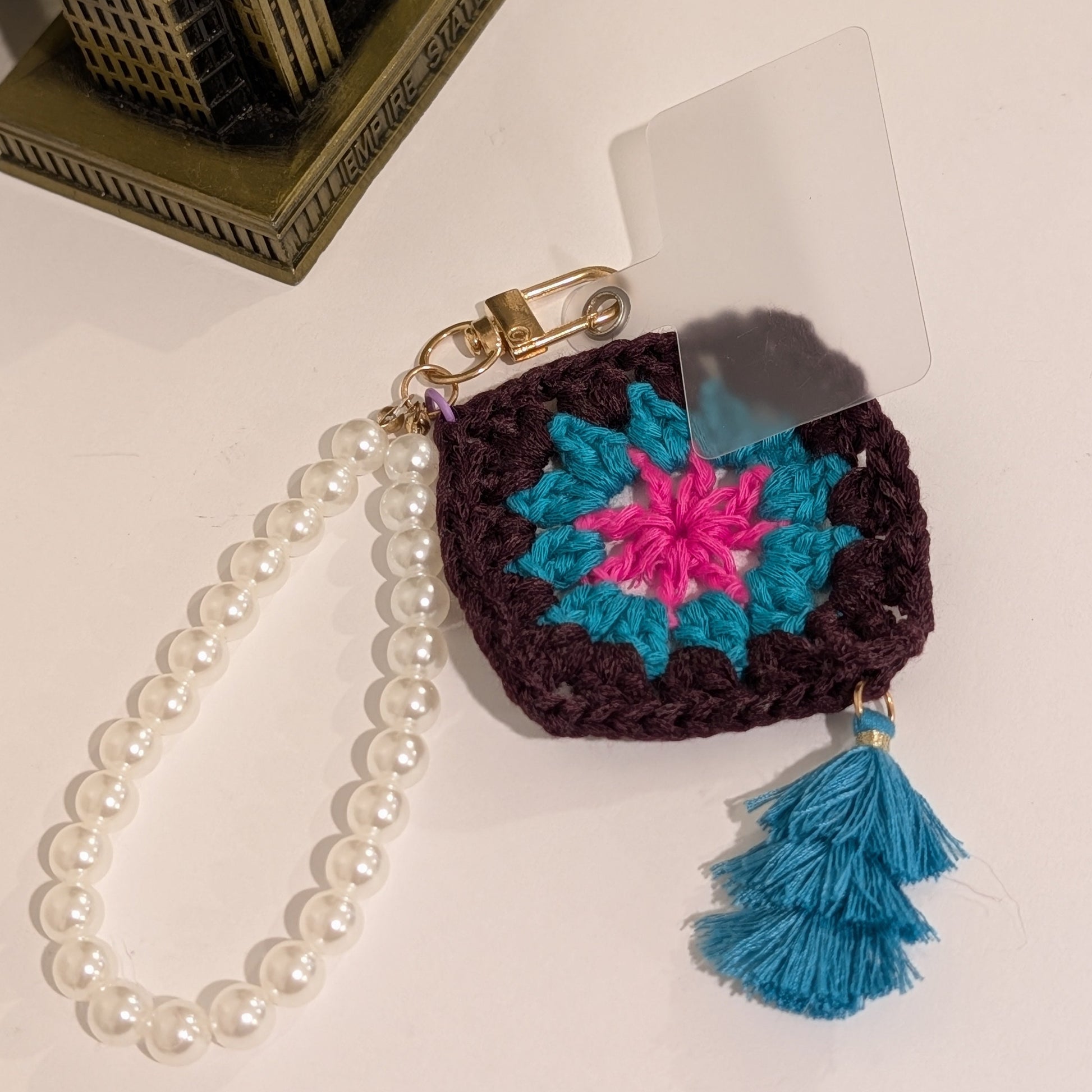Crocheted keychain with colorful design, teal tassel on a white surface