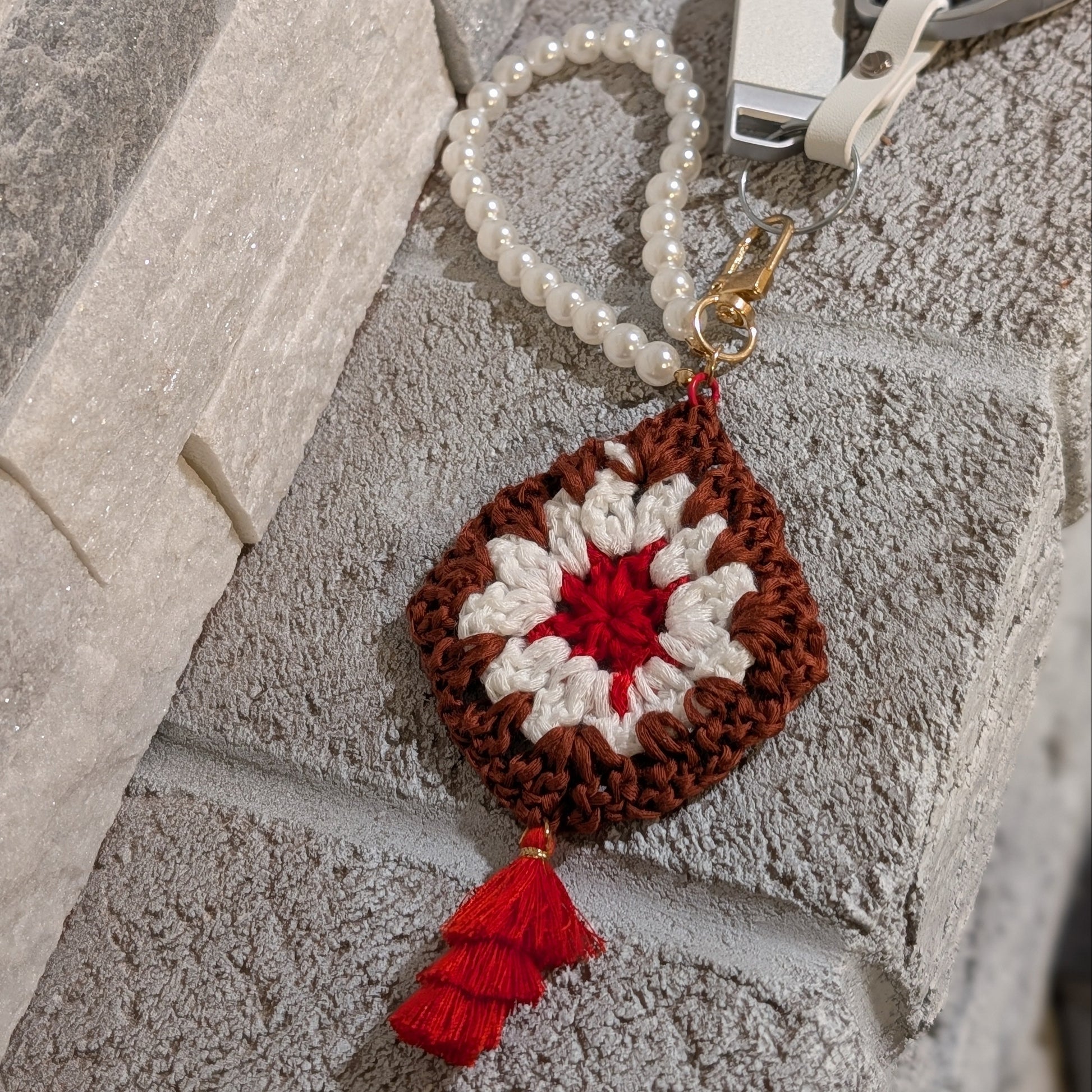 Crocheted keychain with red and white design and red tassel on a textured stone surface