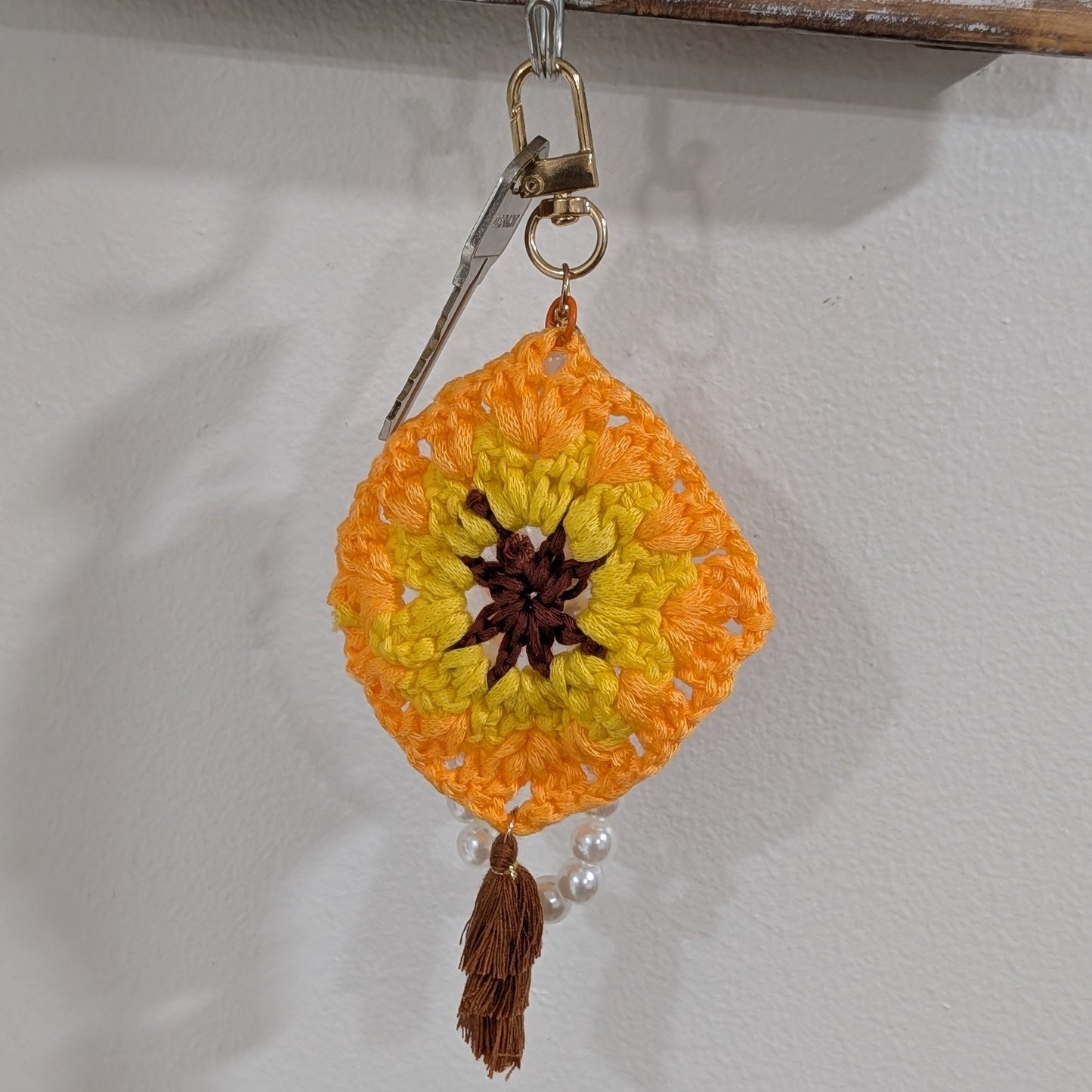 Crocheted orange and yellow keychain and bracelet with a tassel on a neutral background