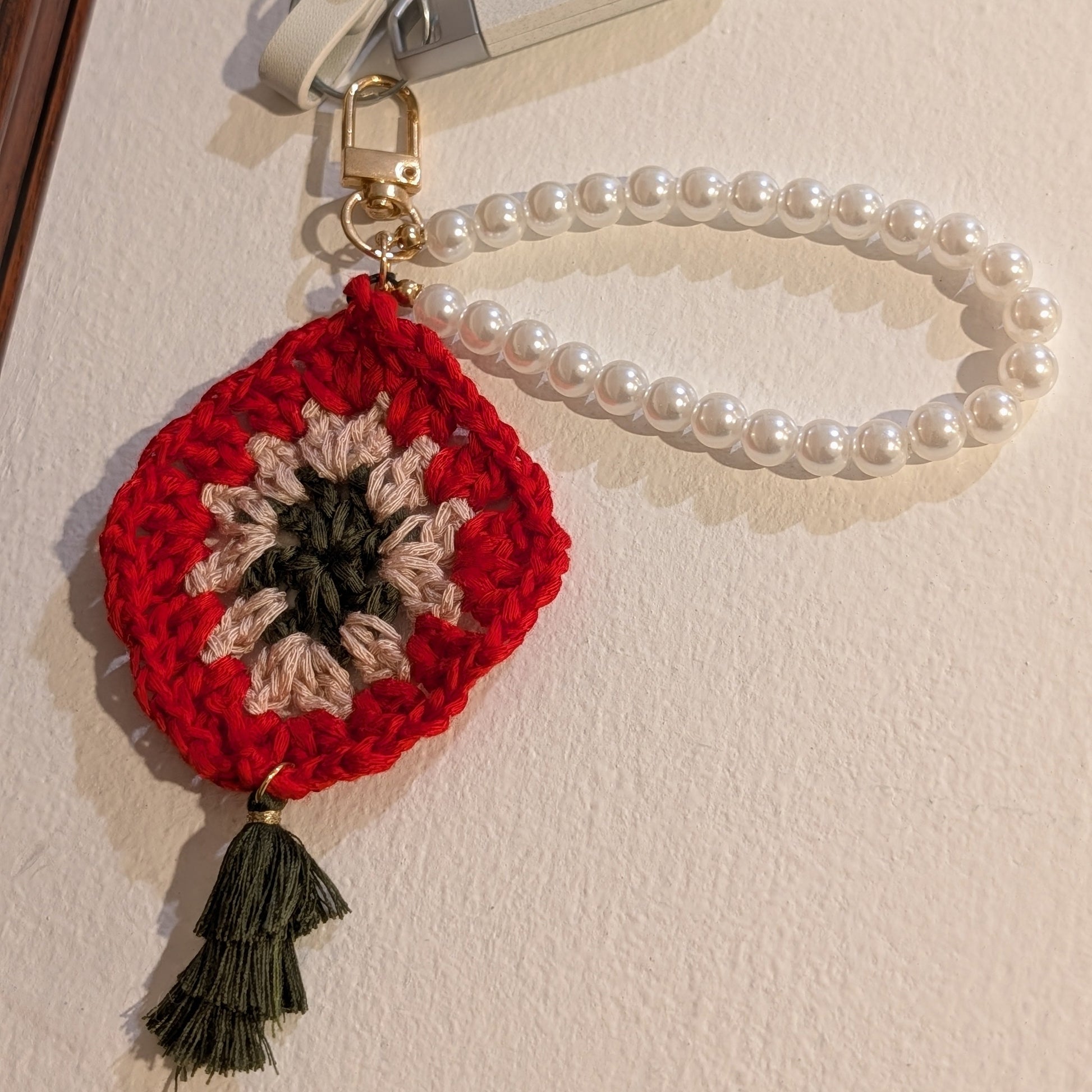 Crocheted red flower keychain with a moss color tassel on a beige background