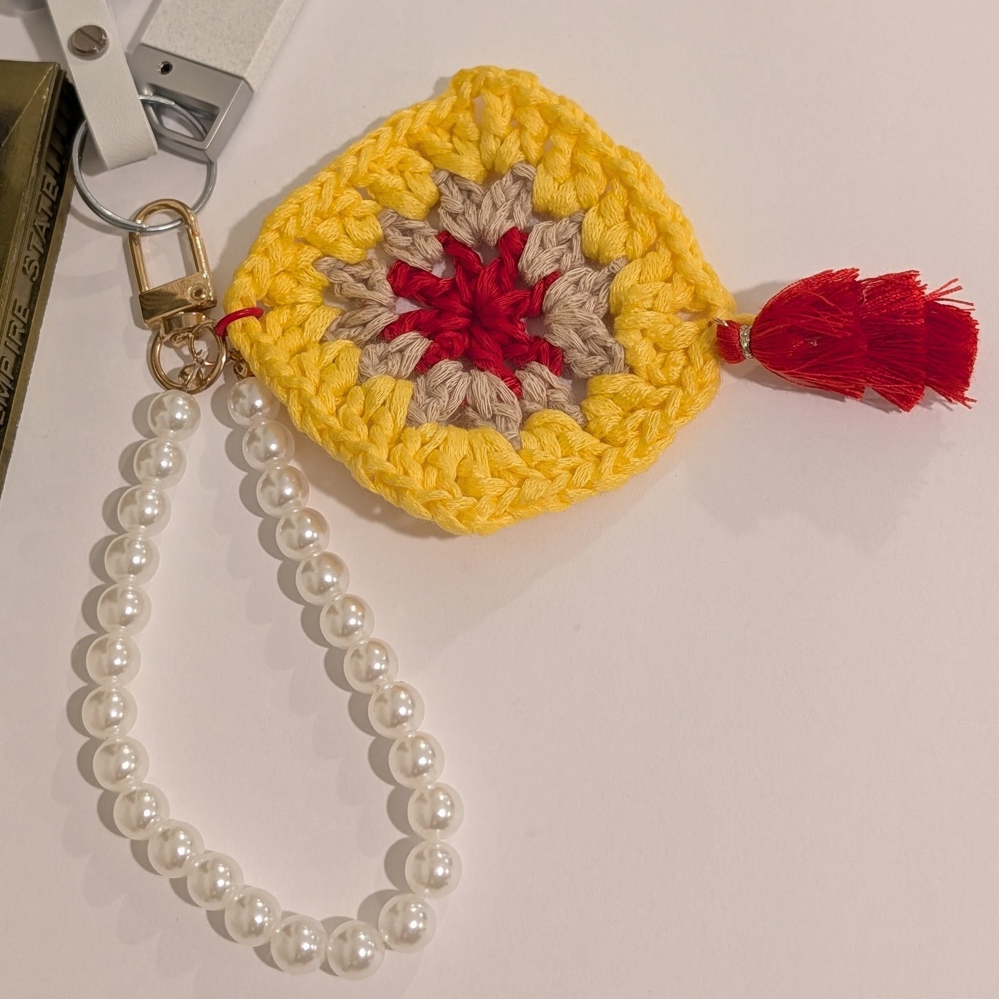 Crocheted yellow keychain with red & gray center and beaded bracelet on a white surface