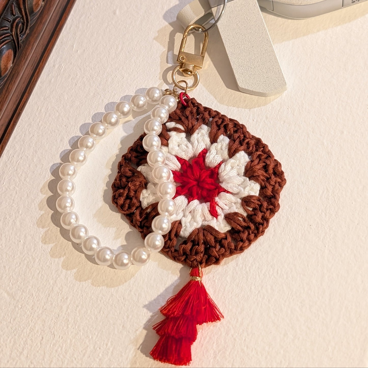 Decorative maroon crochet flower keychain with red tassel on a beige surface