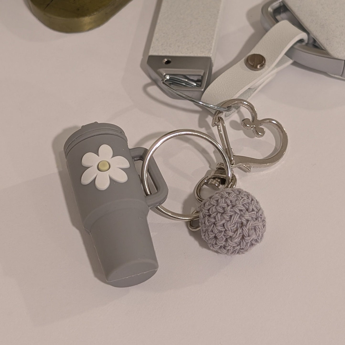Gray silicone Keychain with black tumbler, flower charm, and pom-pom attached to a car key on a light surface.