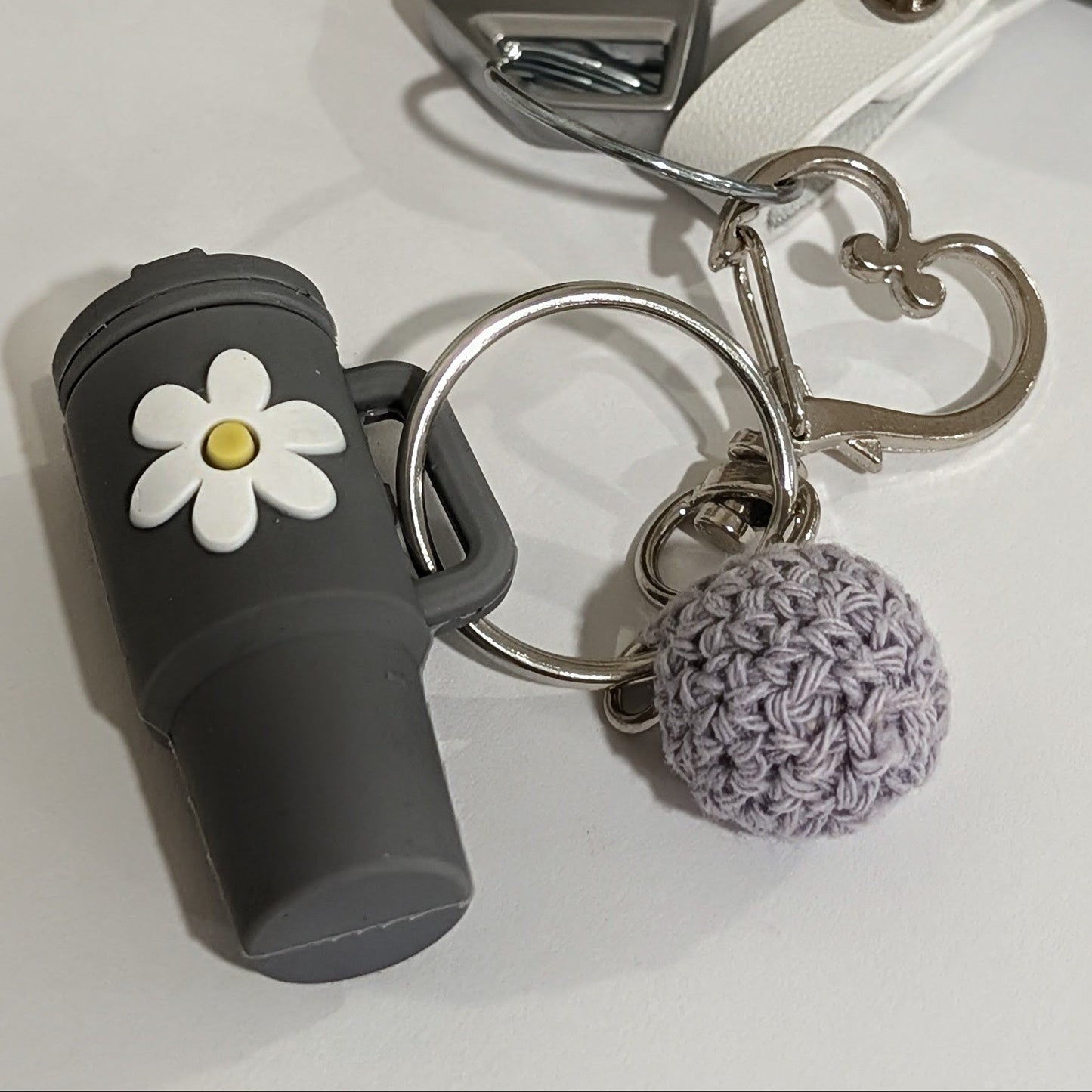 Gray silicone Keychain with black tumbler, white flower charm, and pom-pom attached to a car key on a light surface.