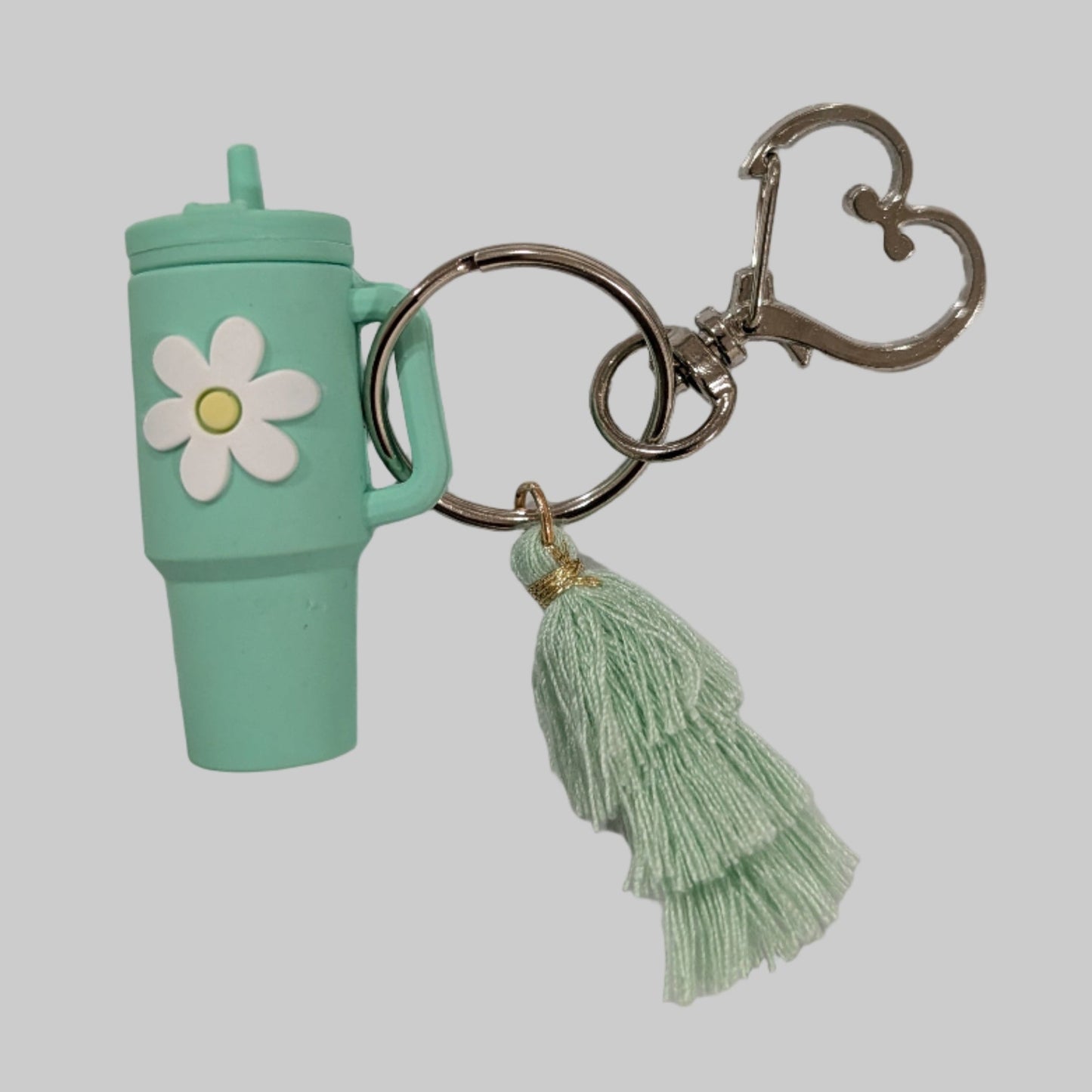 Green tumbler cup-shaped keychain with a flower and tassel on a light gray background
