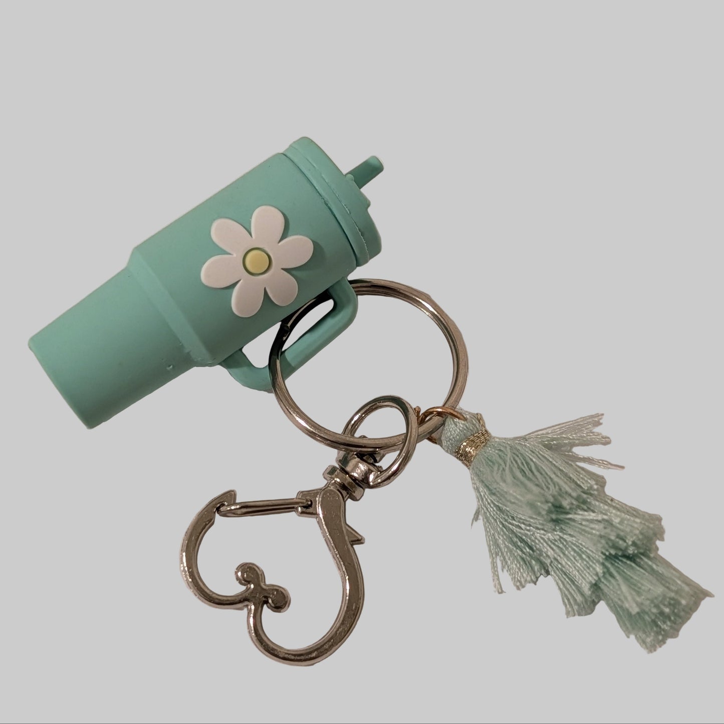 Green tumbler cup-shaped keychain with a flower and tassel on a white background