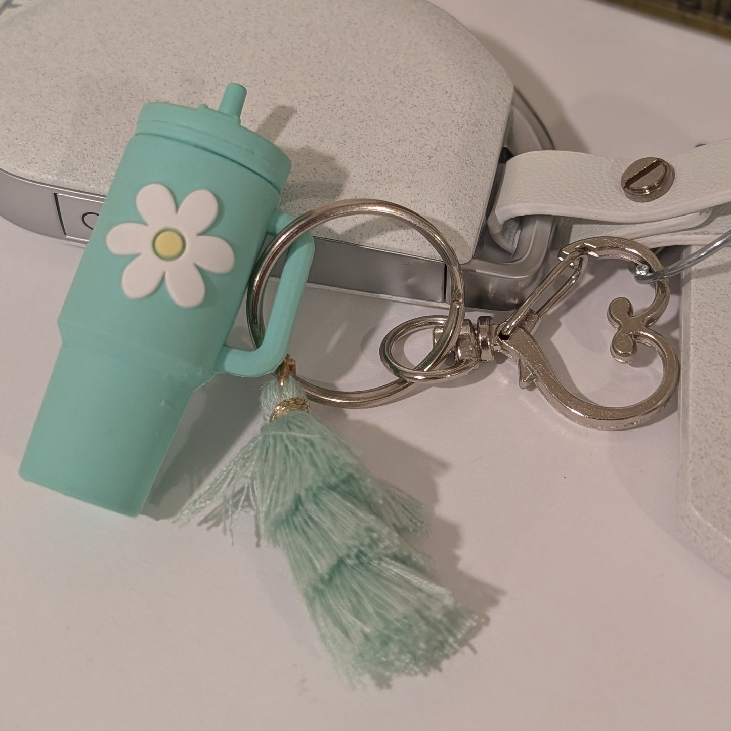 Green tumbler cup-shaped keychain with a flower and tassel attached to a car key on a light white background