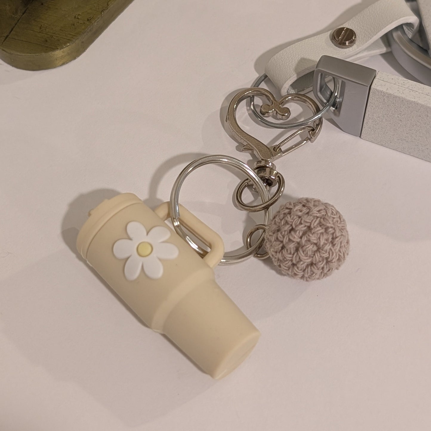 Keychain with a Beige silicone tumbler charm and crochet ball attached to a car key on a white surface