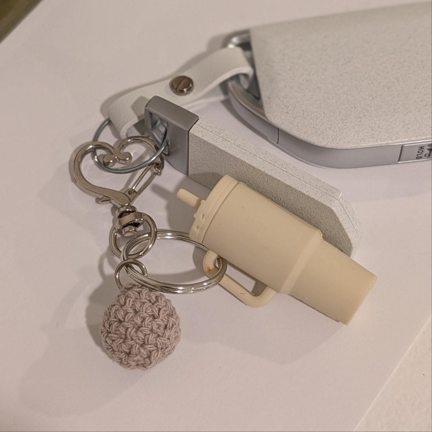 Keychain with a Beige silicone tumbler with white flower charm and crochet ball attached to a car key on a white surface