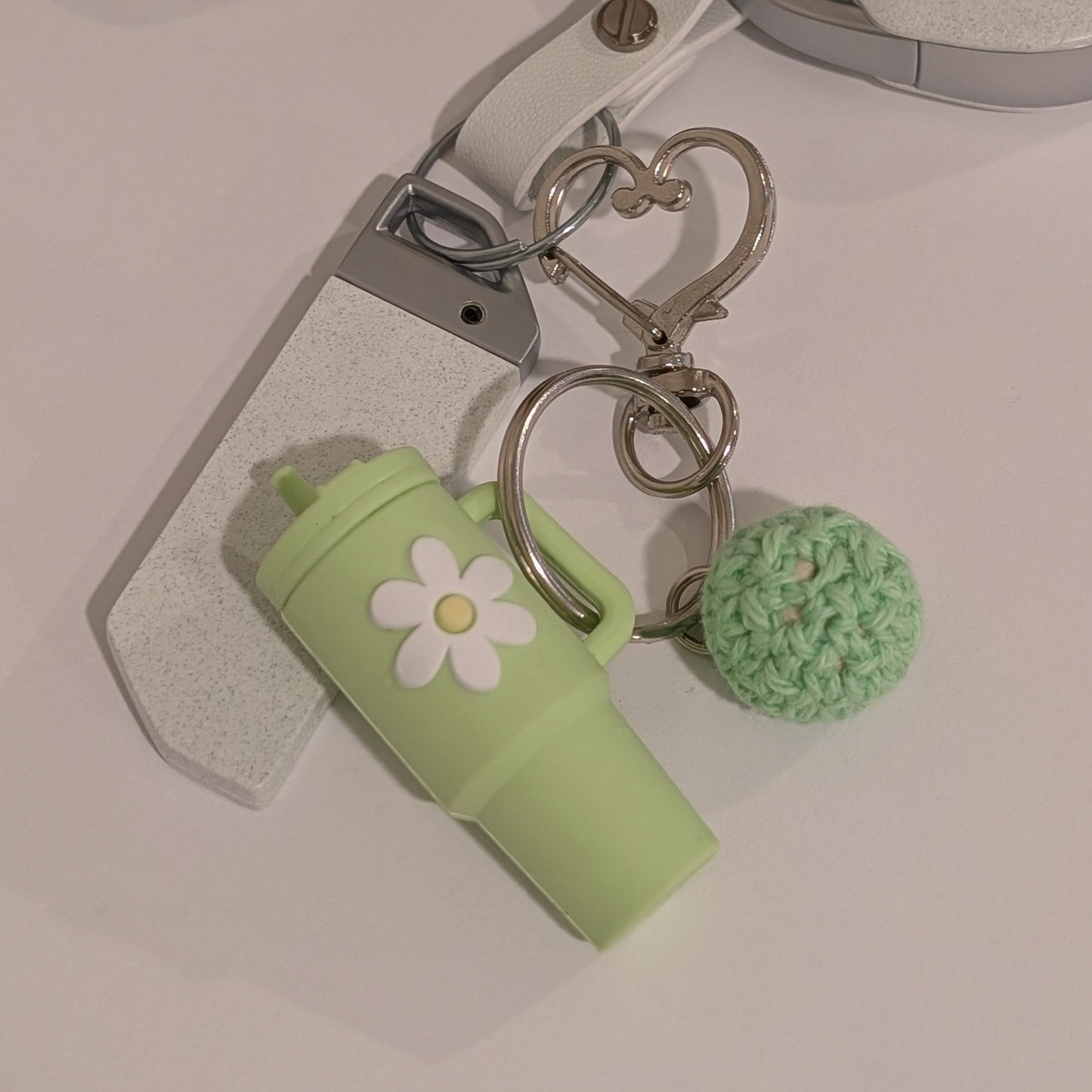 Keychain with a green silicone tumbler charm and crochet ball on a white surface
