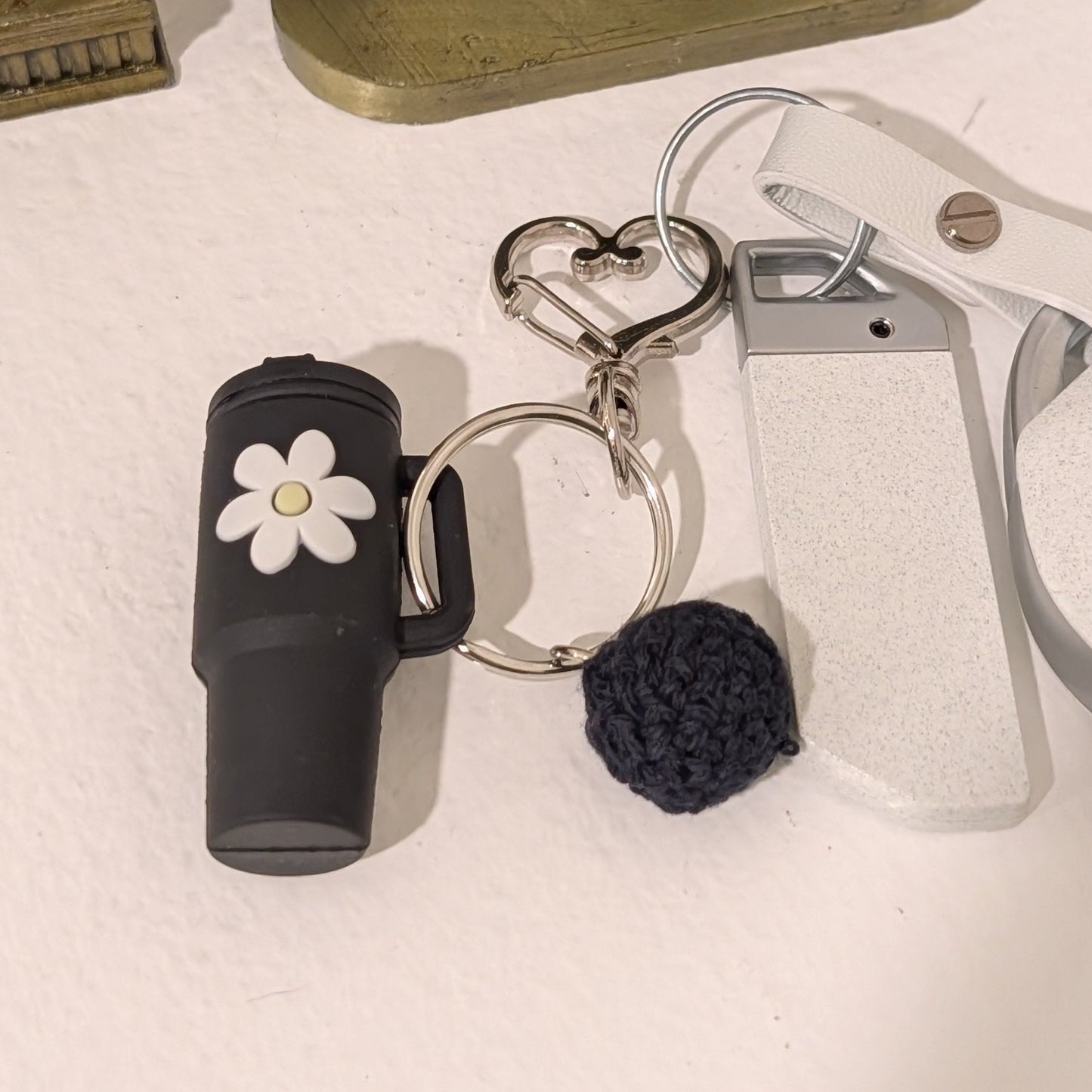 Keychain with black silicone tumbler, flower charm, and crochet ball attached to car key on a light surface.
