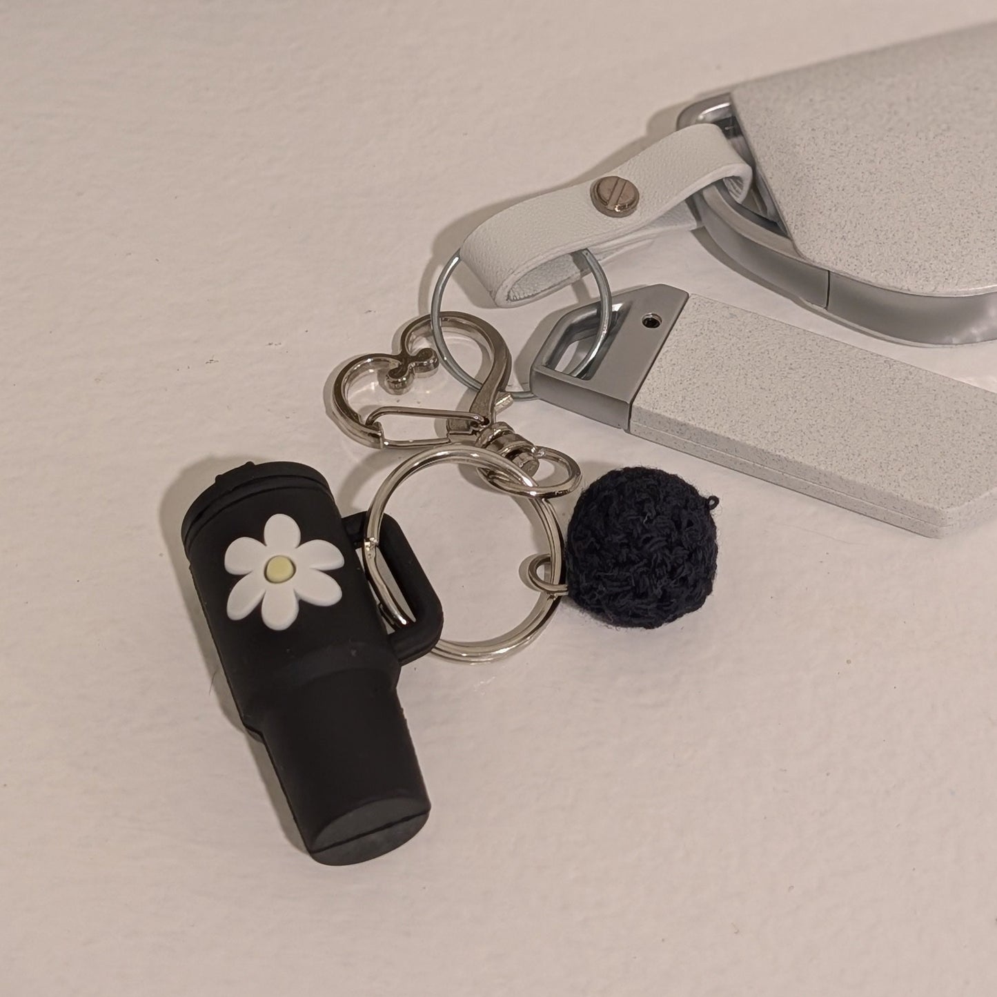 Keychain with black silicone tumbler, flower charm, and pom-pom attached to car key on a light surface.