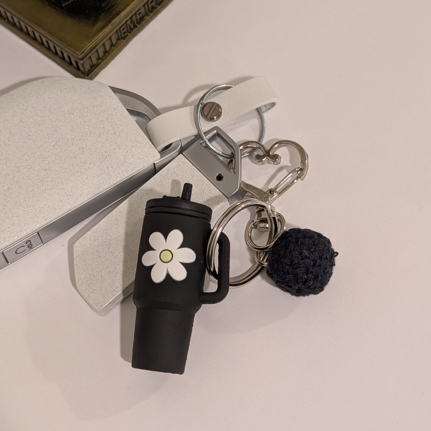 Keychain with black tumbler, flower charm, and pom-pom on a light surface.