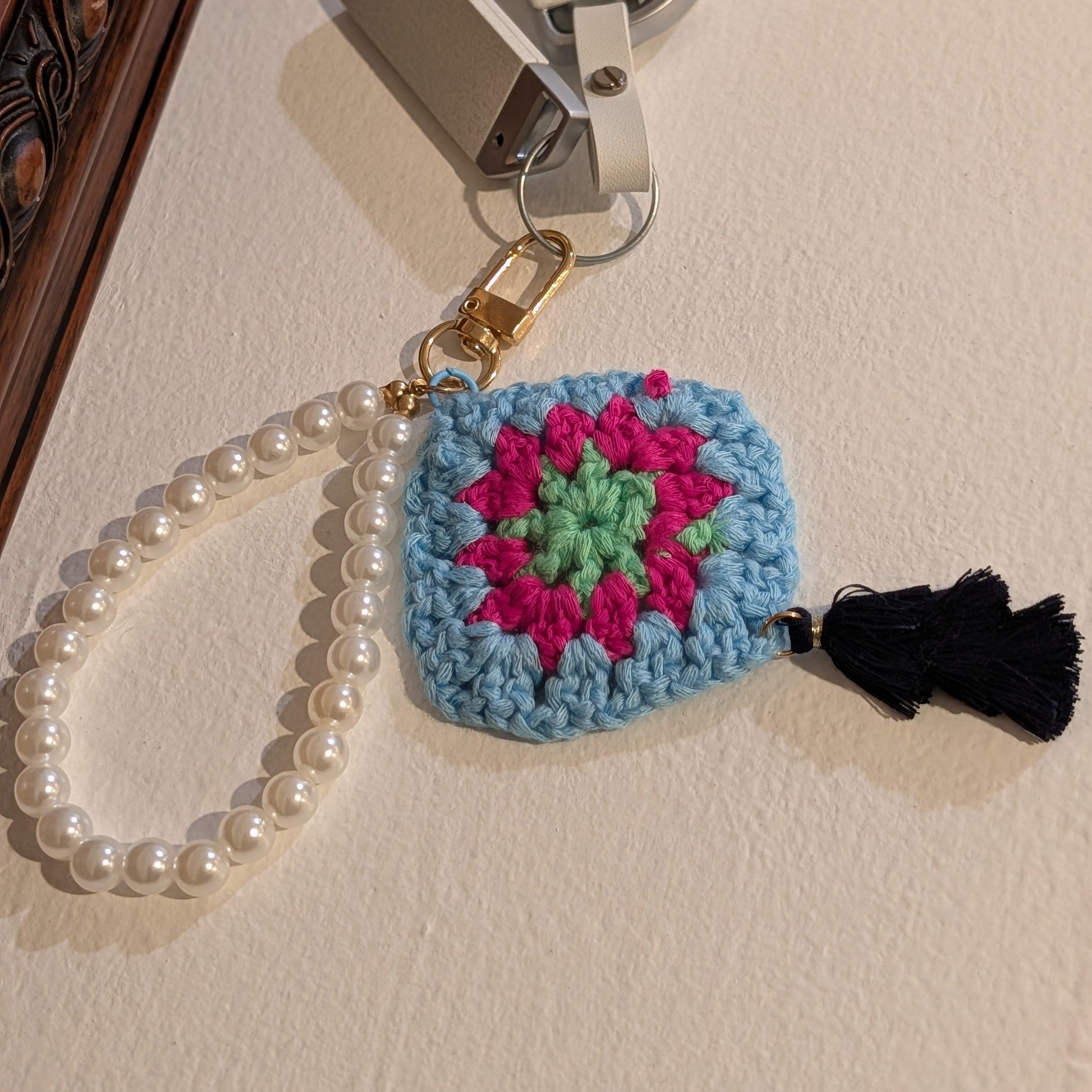 Keychain with blue crochet square and black tassel on a white wall