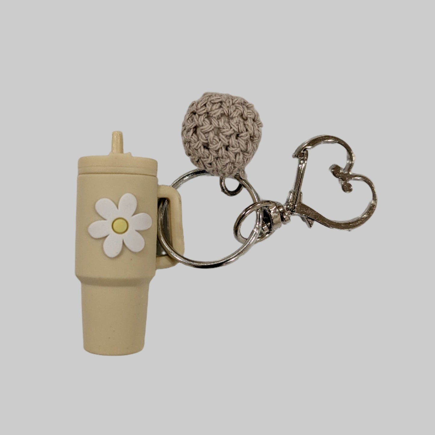 Keychain with little beige silicone tumbler, white flower, and textured ball on a light gray background