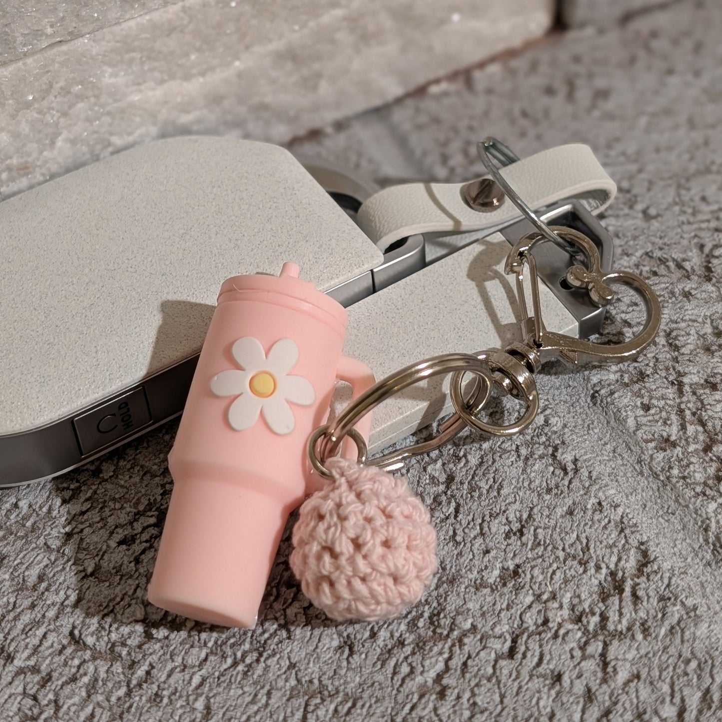 Light pink silicone tumbler key chain with crochet ball and heart shaped hook attached to a car key on a gray surface