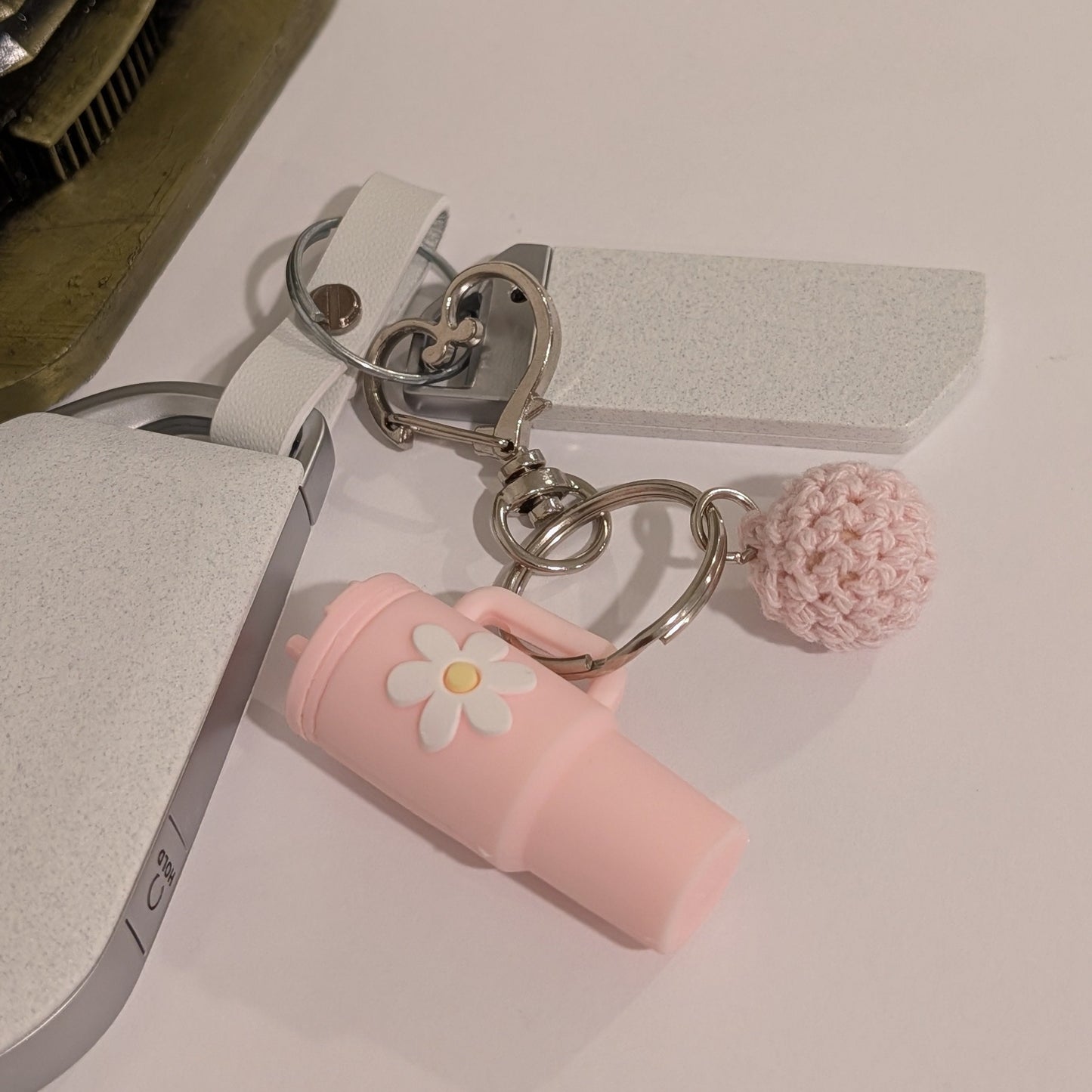 Light pink silicone tumbler key chain with crochet ball and heart shaped hook attached to a car key on a white surface next to an ornament