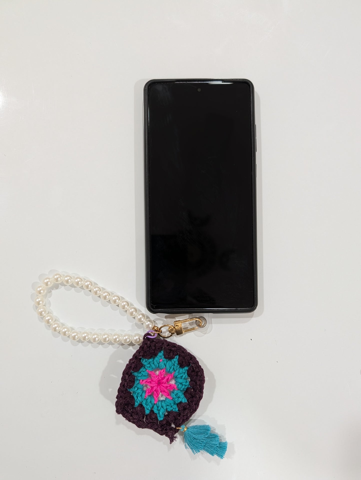 Phone with a crocheted charm keychain and beads bracelet on a white background