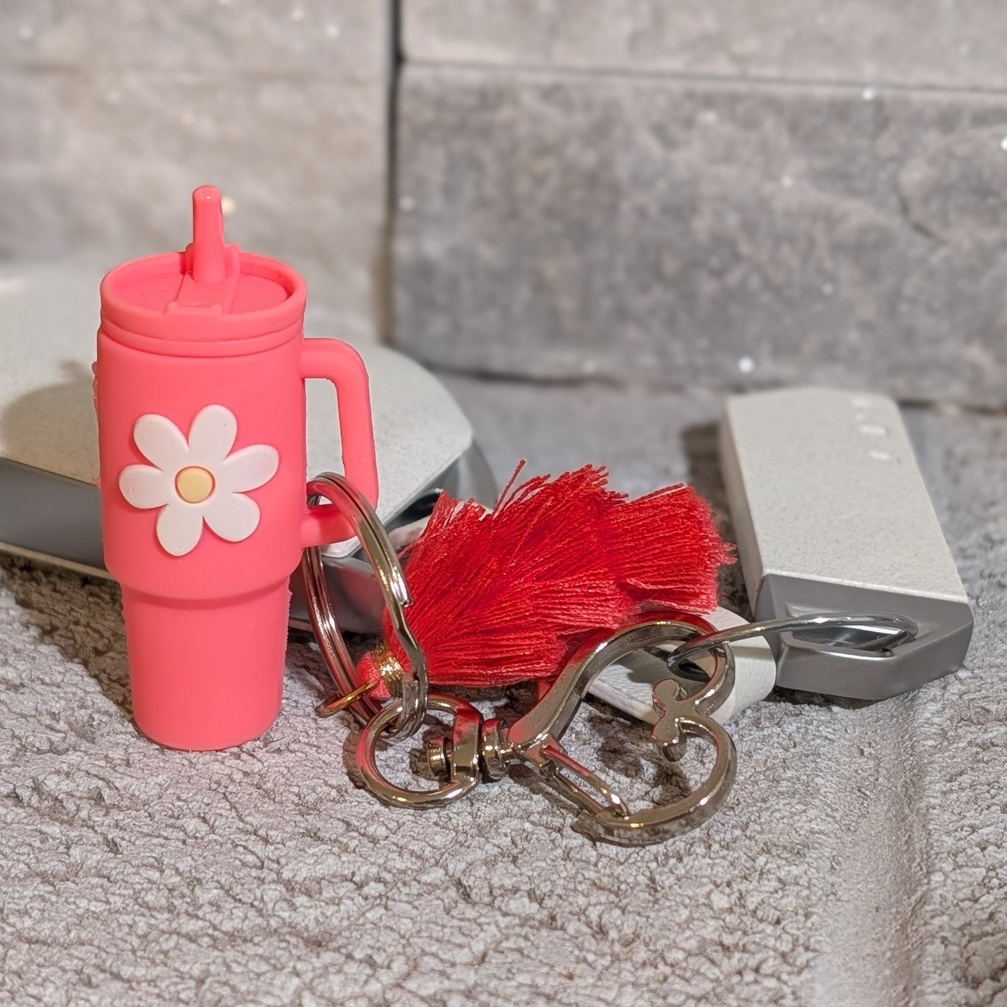 Pink keychain with a flower charm, heart shaped buckle and red tassel attached to a car key on a gray background