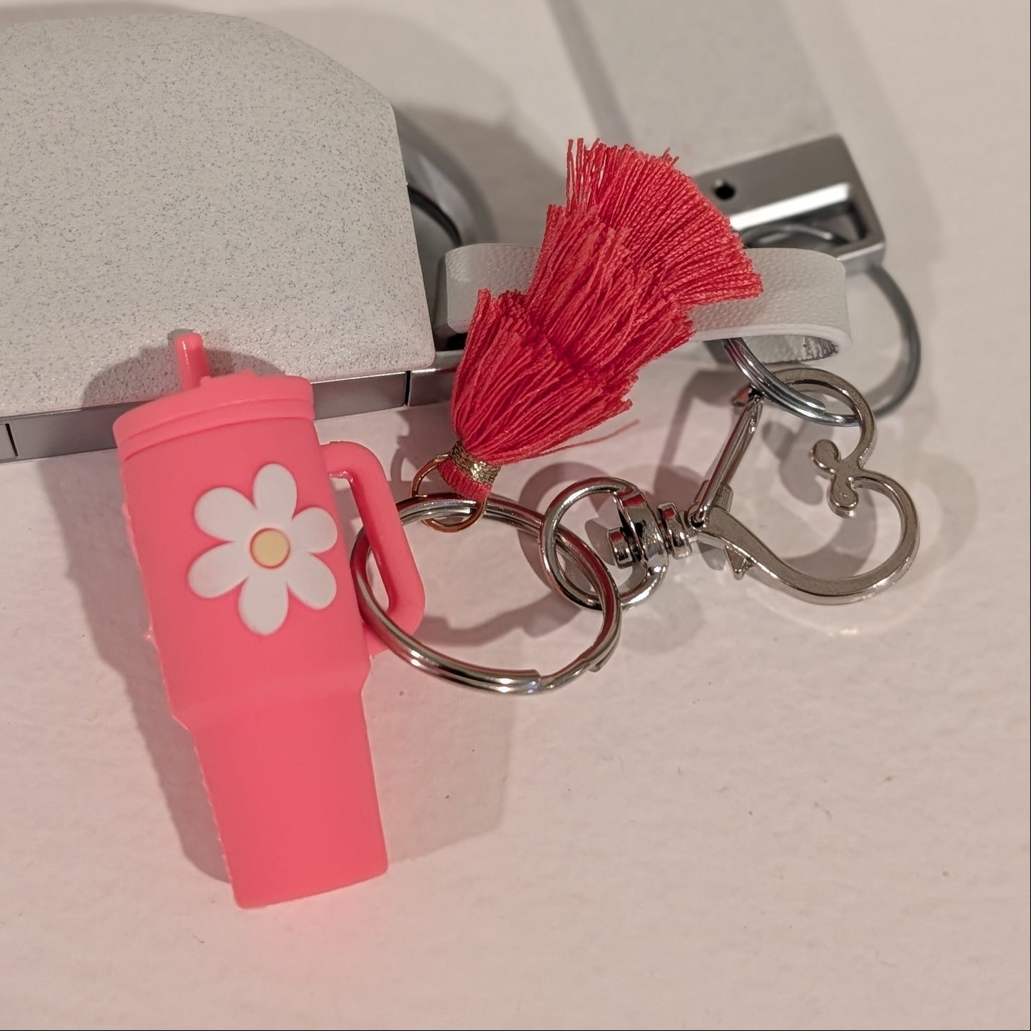 Pink keychain with a flower charm, heart shaped buckle and red tassel attached to a car key on a light background