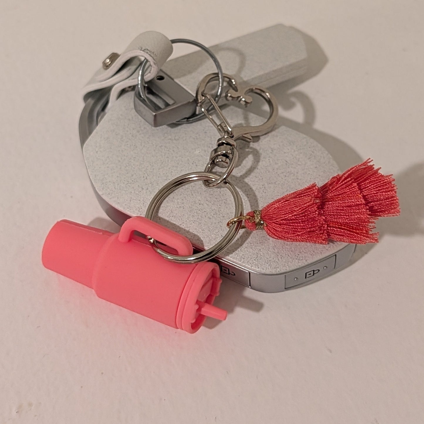 Pink keychain with a flower charm, heart shaped buckle and red tassel attached to a car key on a white background