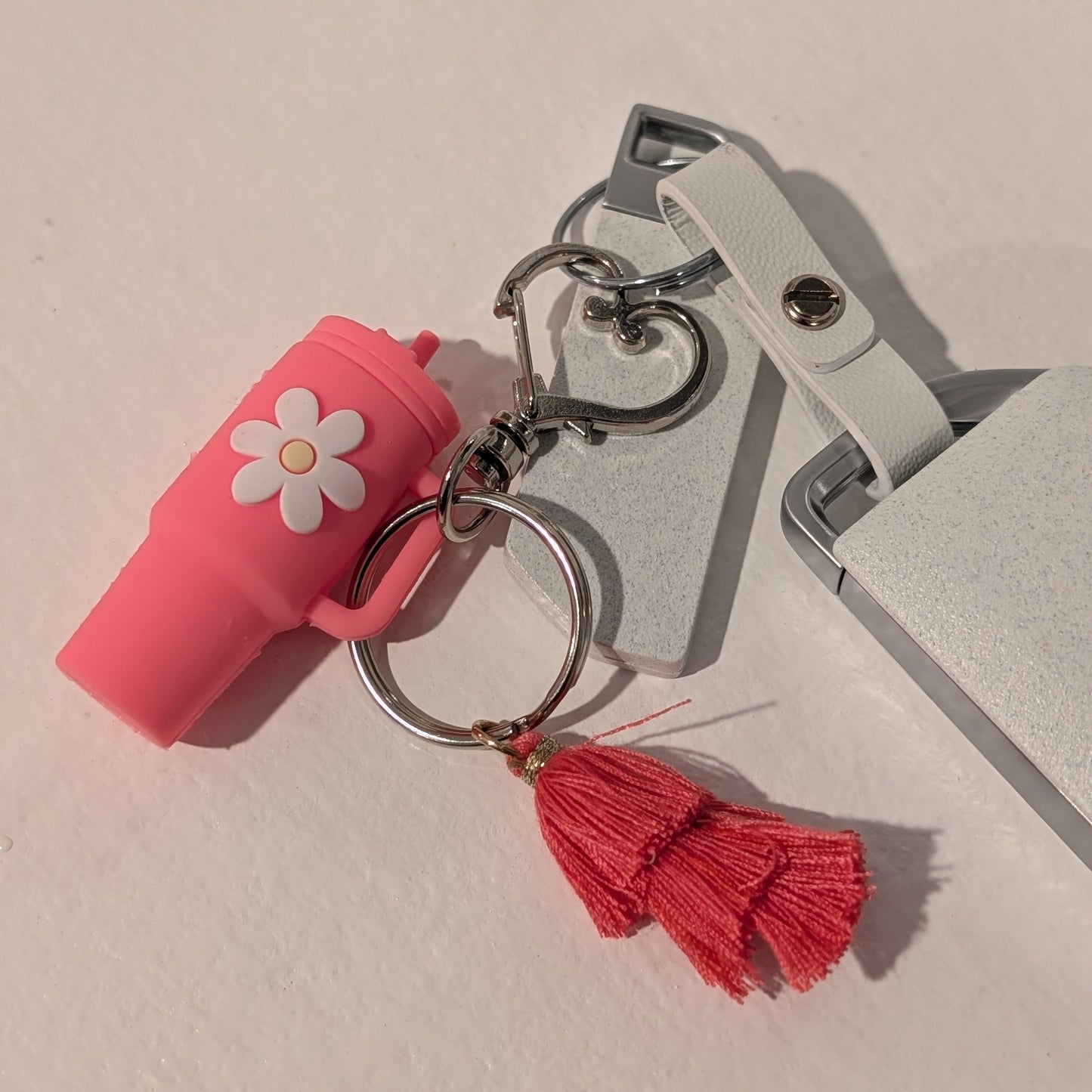 Pink keychain with a flower charm, heart shaped buckle and red tassel on a light background