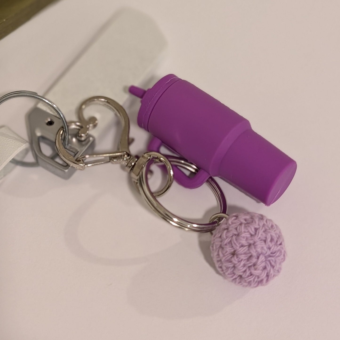Purple silicone Keychain with black tumbler, flower charm, and pom-pom attached to a car key on a light surface.