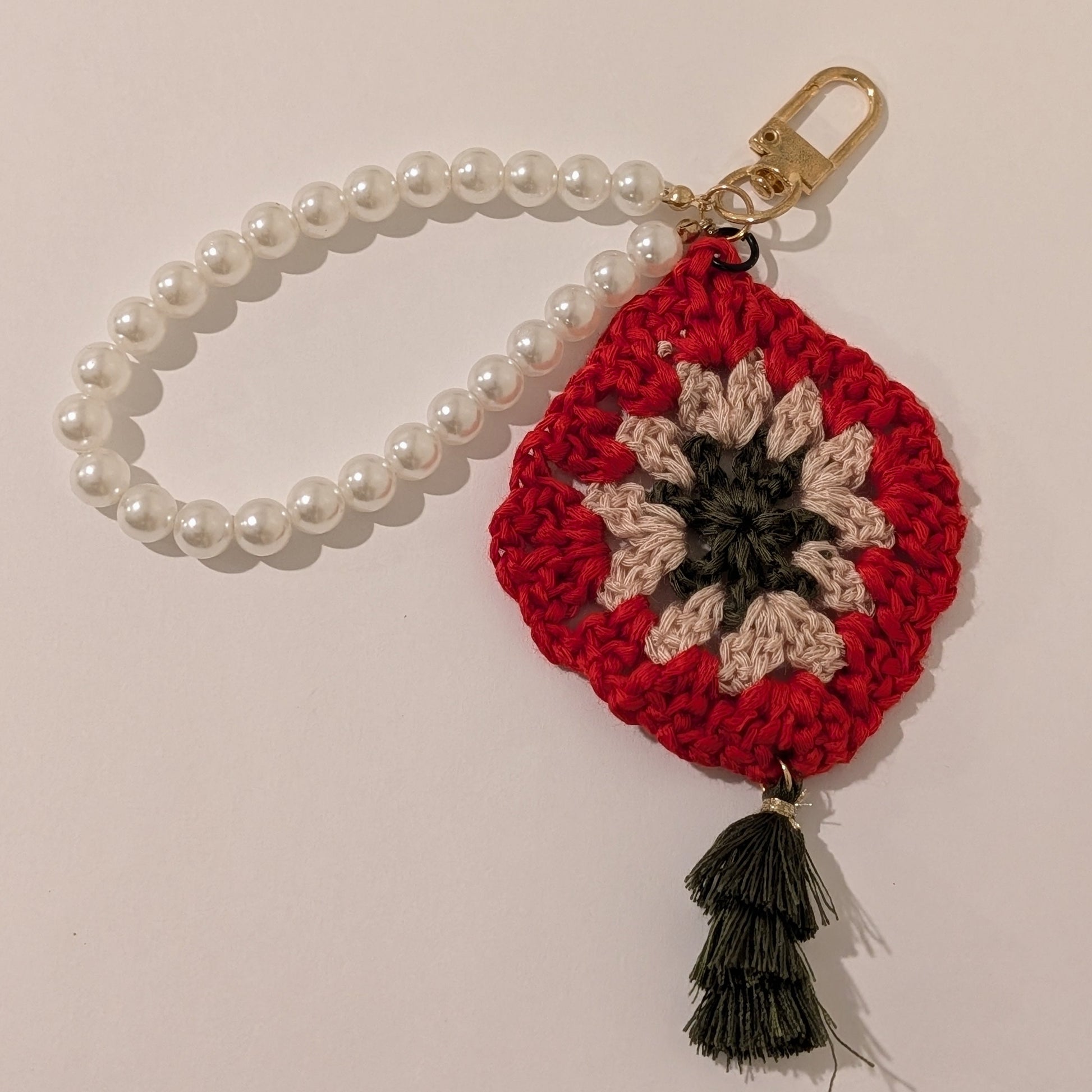 Red crocheted keychain with floral design, pearl bracelet chain and moss color tassel on a beige background