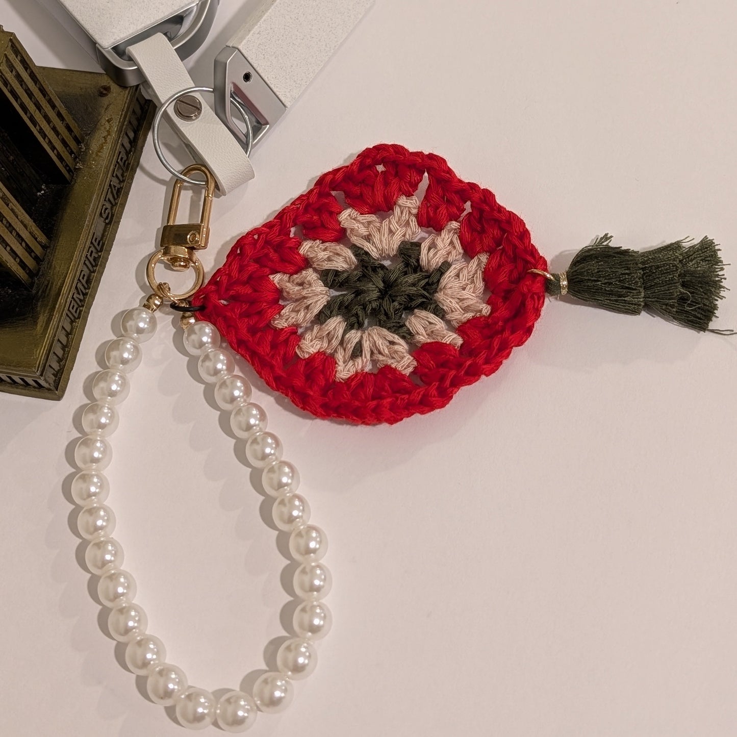 Red crocheted keychain with floral design, white pearl bracelet and tassel on a white background