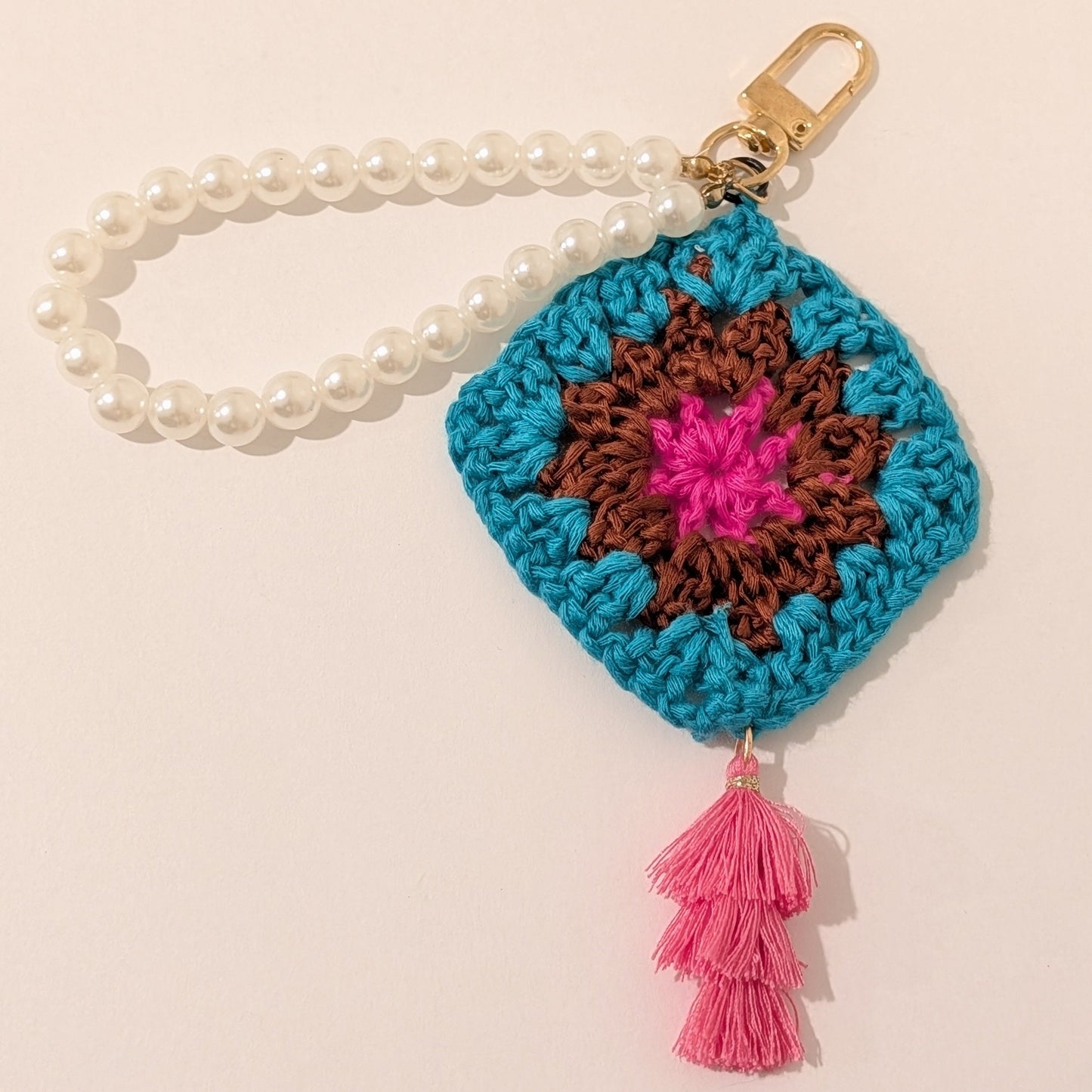 Teal crocheted keychain with colorful design, white pearl bracelet on a beige background