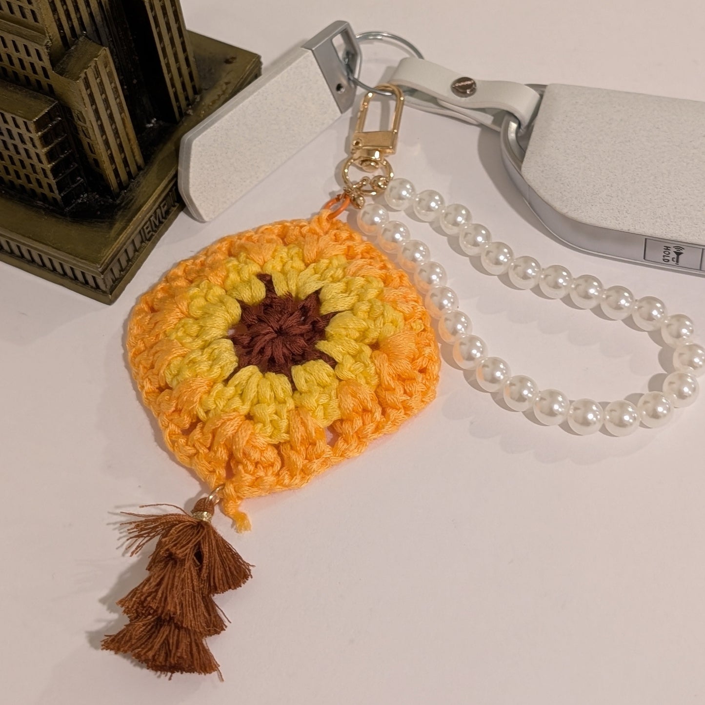 Yellow Crocheted flower keychain with brown tassel and a pearl bracelet attached to a car key on a white surface