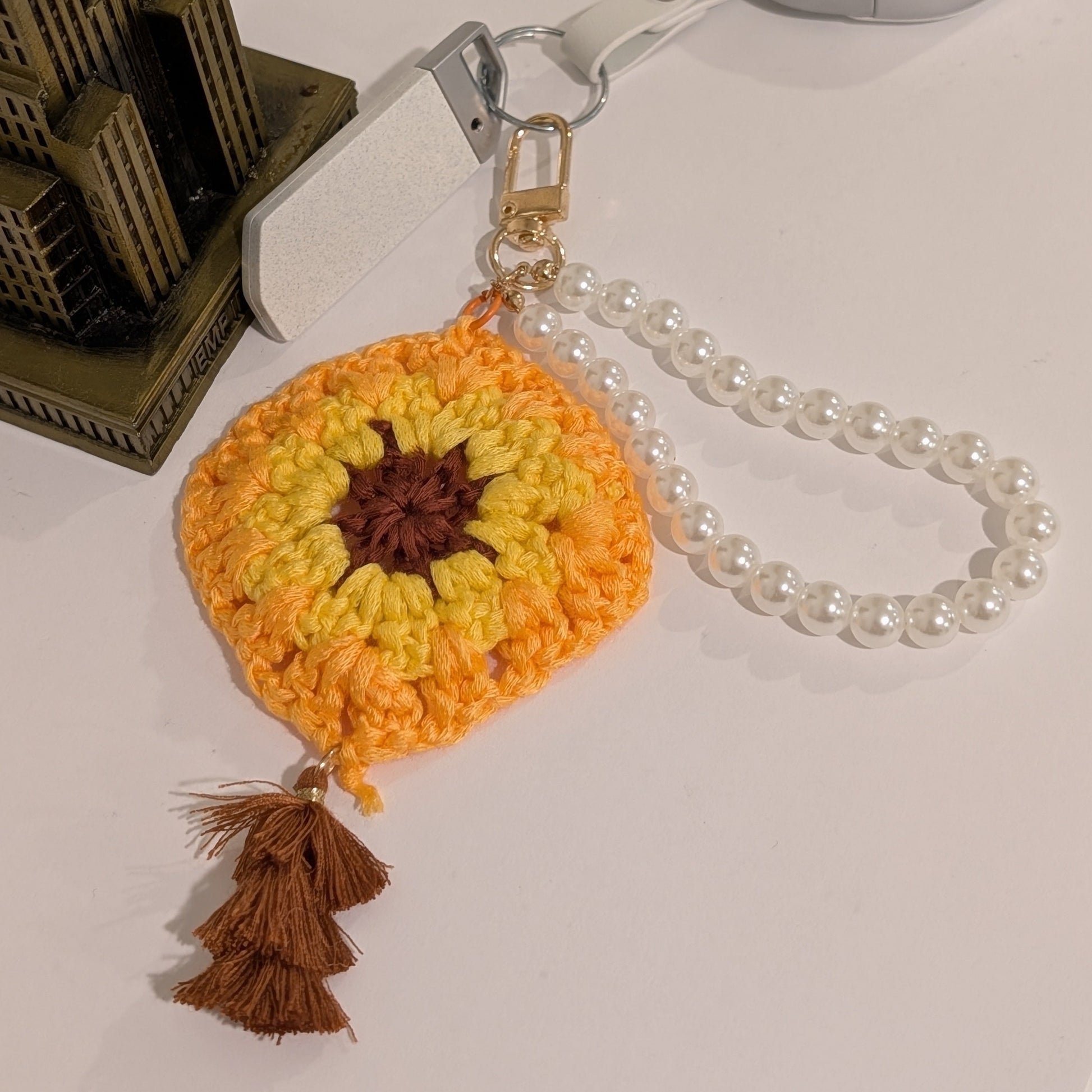 Yellow Crocheted flower keychain with brown tassel and white beaded bracelet on a white surface.
