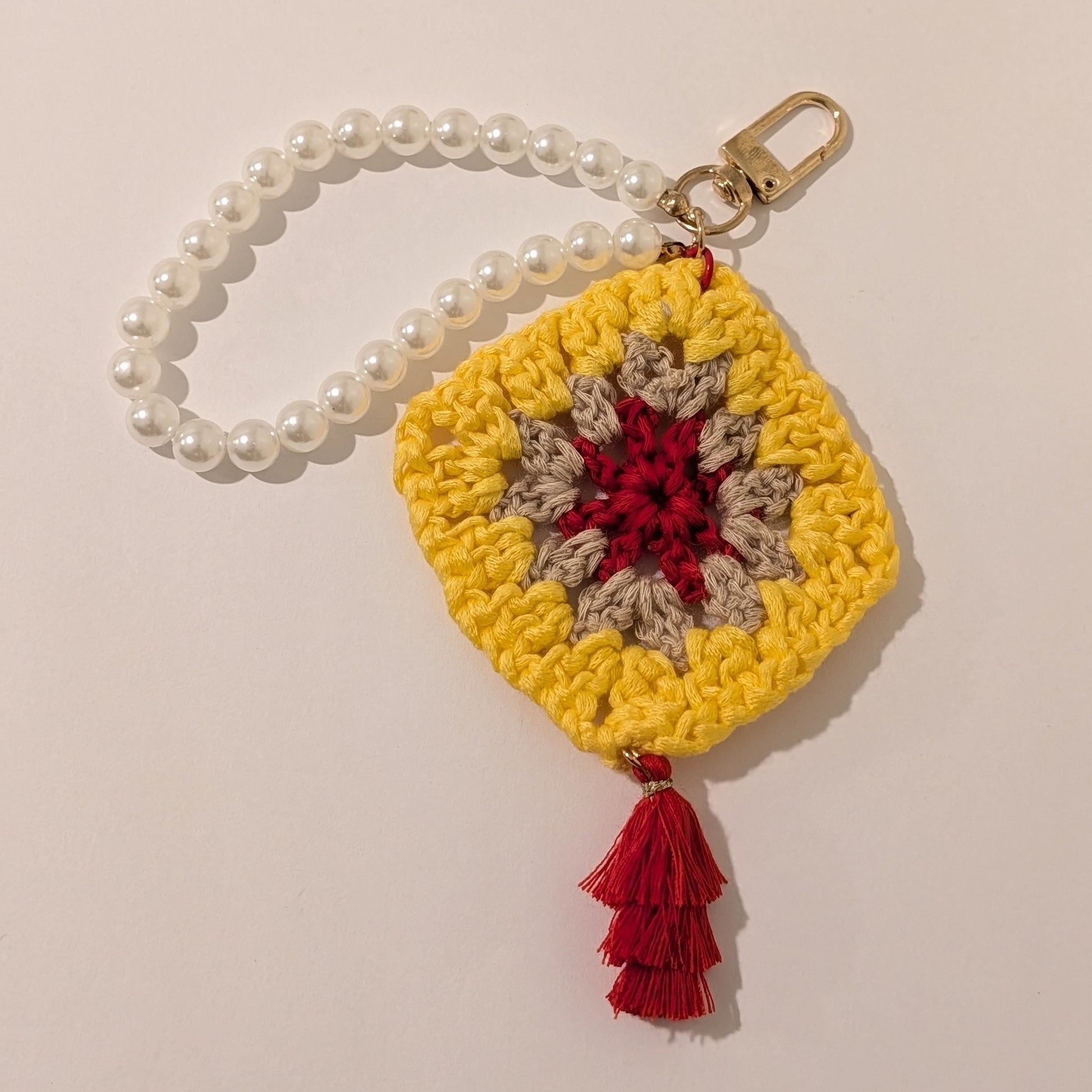 Yellow Crocheted keychain with a red center, red tassel and beaded bracelet on a beige background