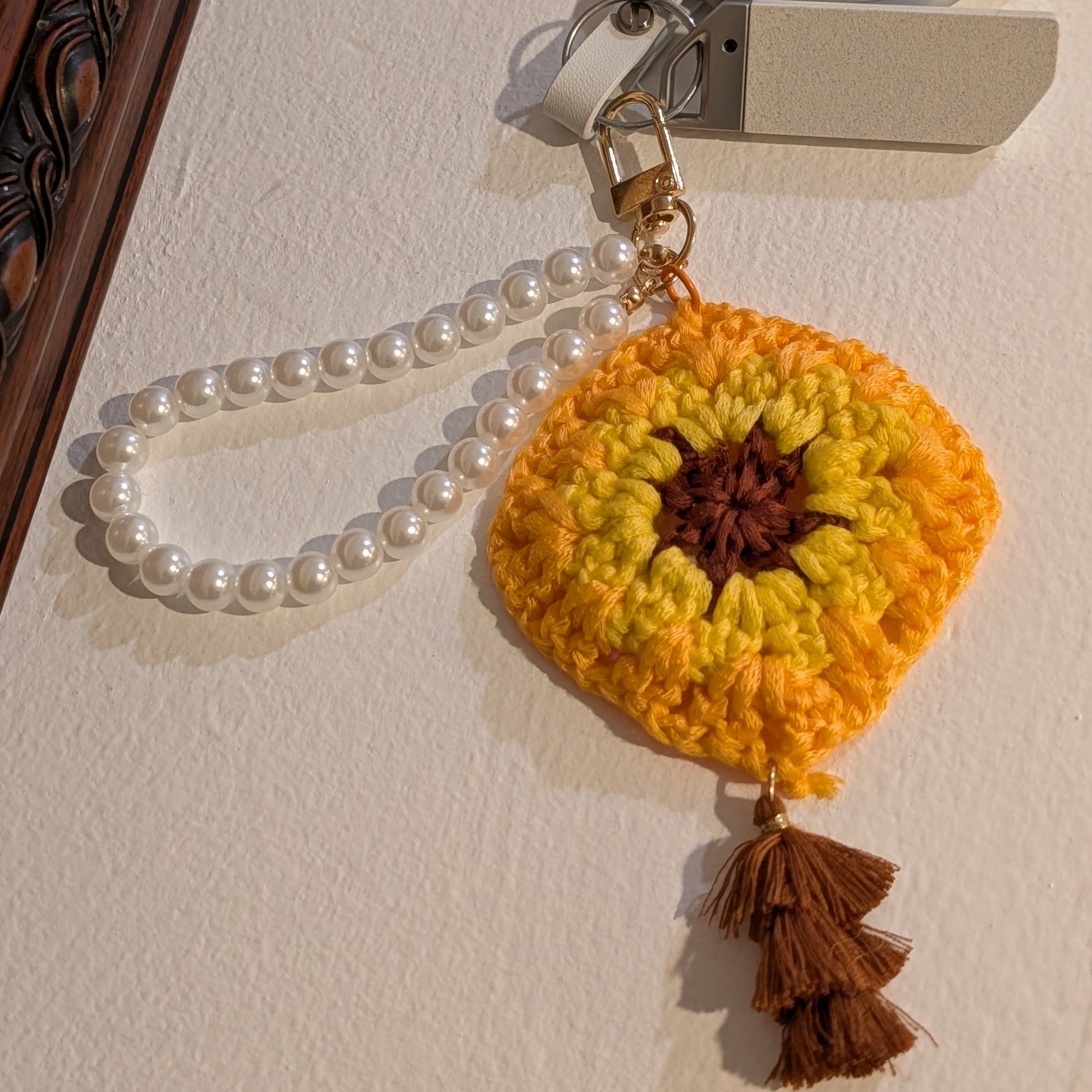 Yellow crocheted keychain with beads attached to a metal clip on a white surface.