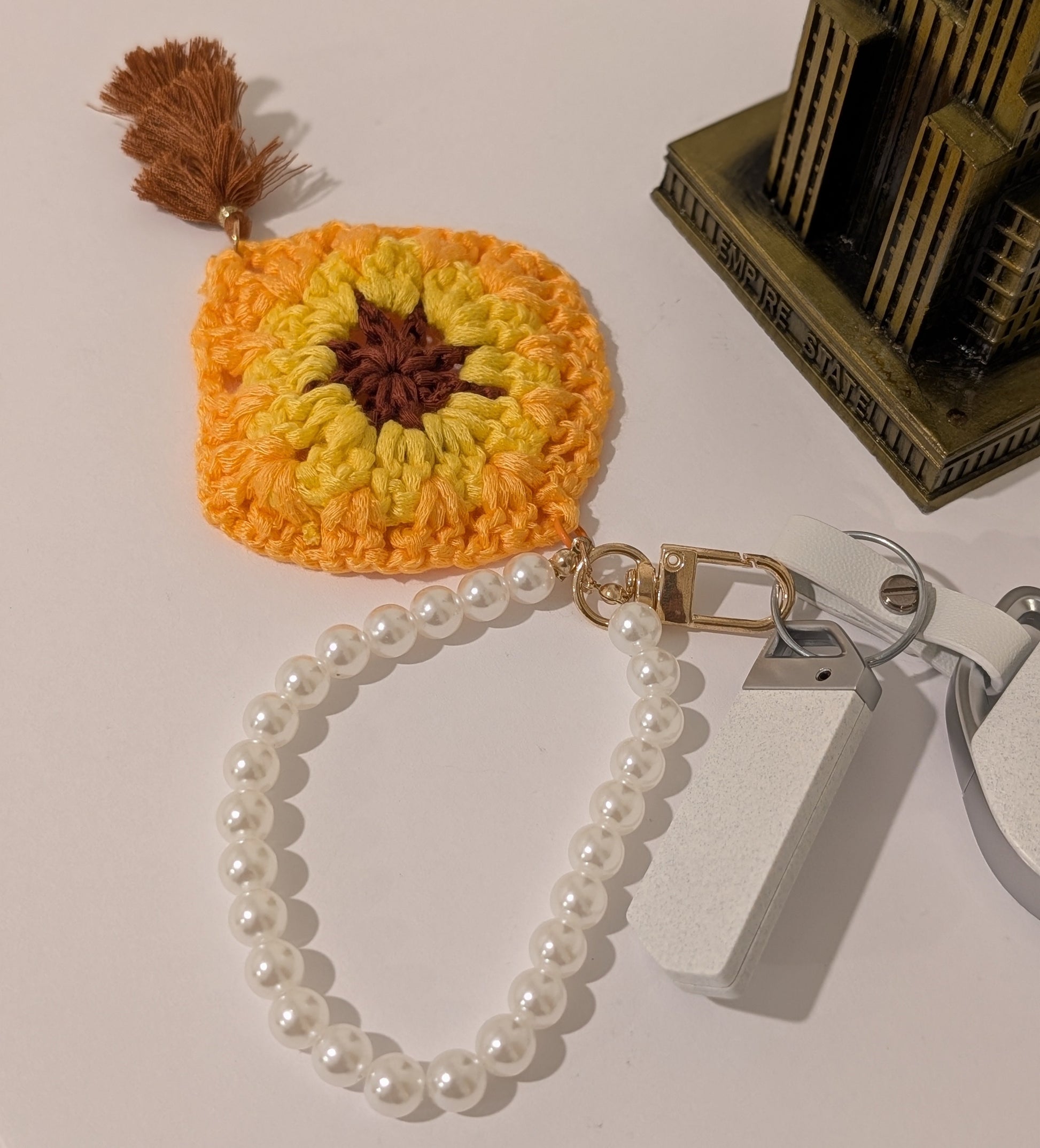 Yellow crocheted keychain with brown tassel and white pearl chain on a white surface
