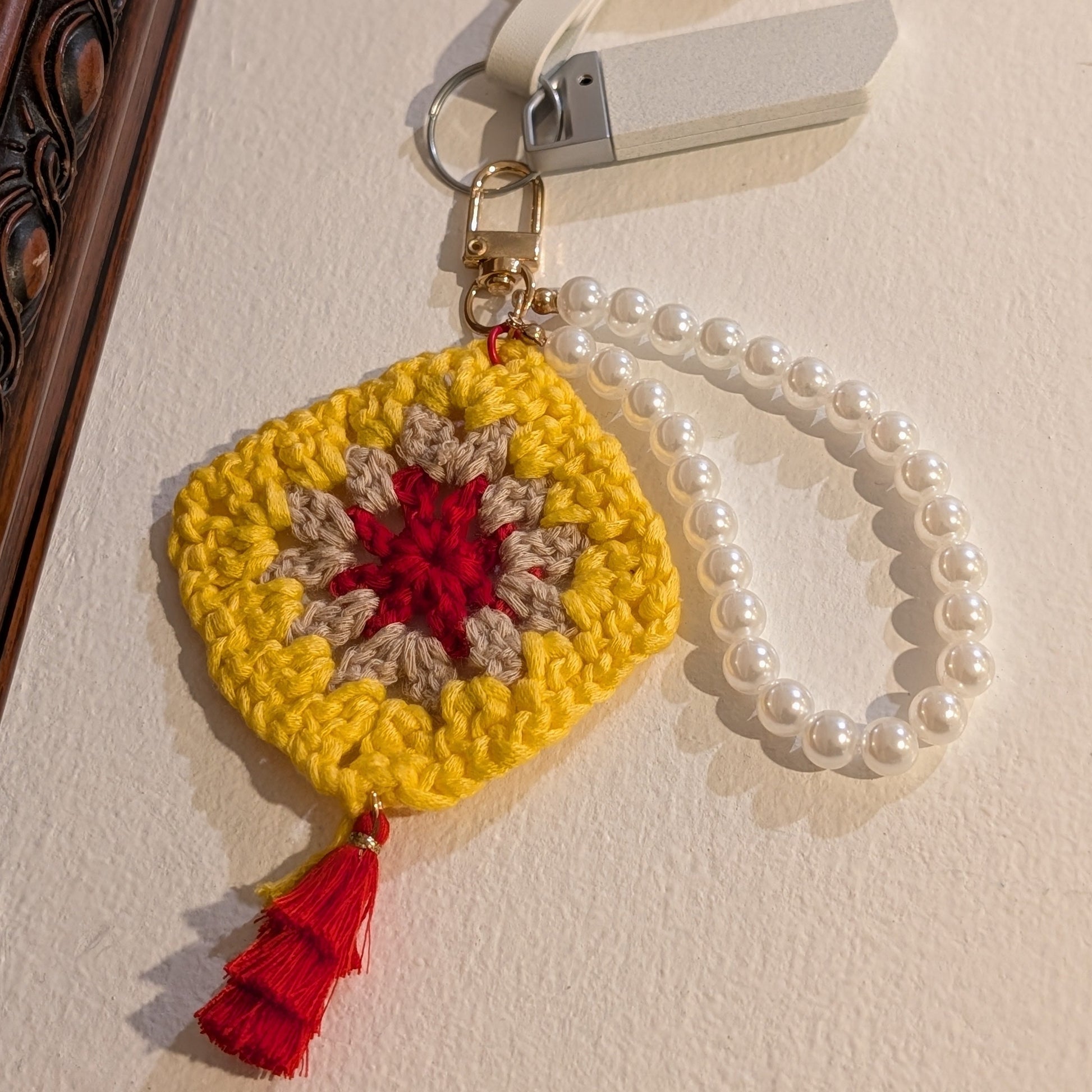 Yellow crocheted keychain with red tassel and pearl bracelet on a white surface.
