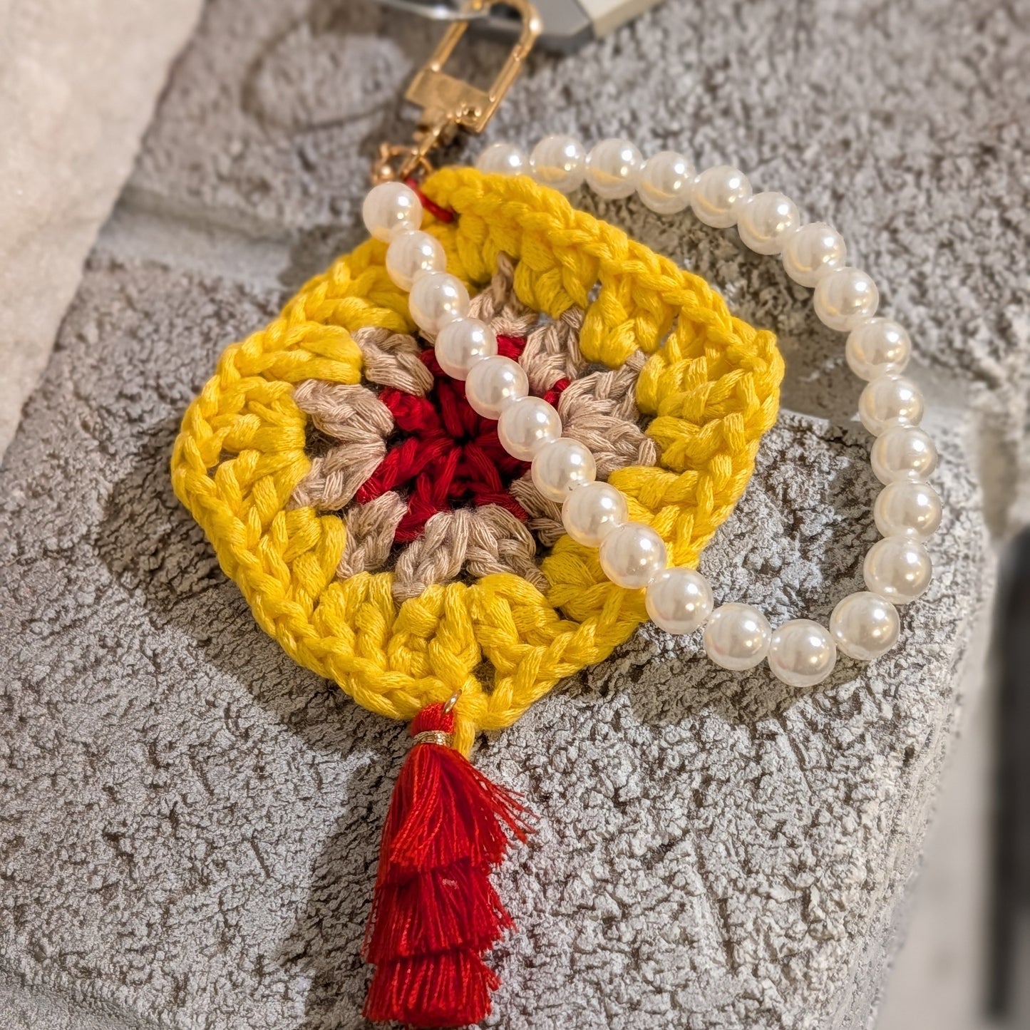 Yellow crocheted keychain with red tassel and pearl bracelet on gray textured surface