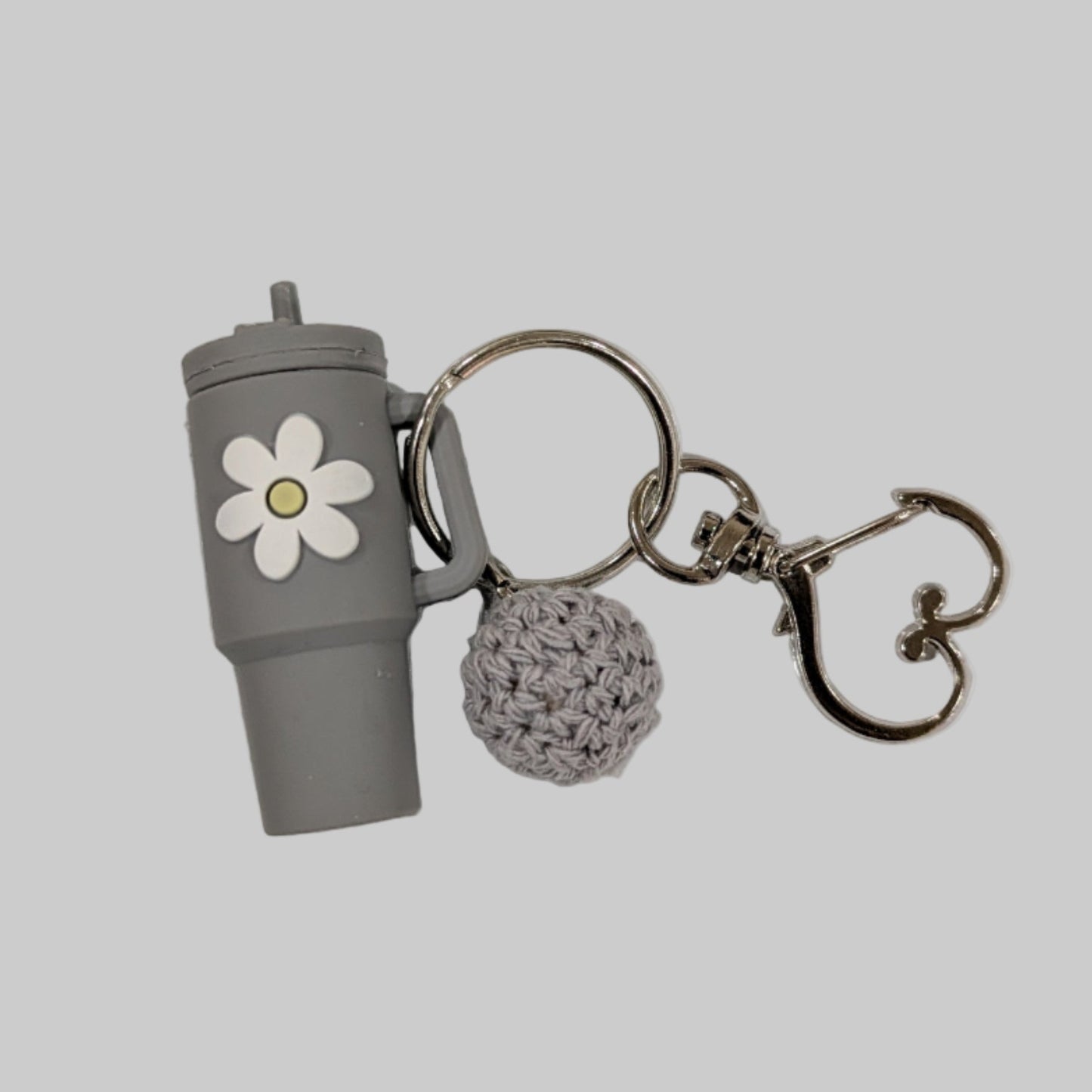 Keychain with a gray cup, white flower, and heart-shaped keychain on a light gray background