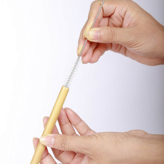 Image to show a reusable bamboo drinking straw being cleaned with a wired cleaning brush.
