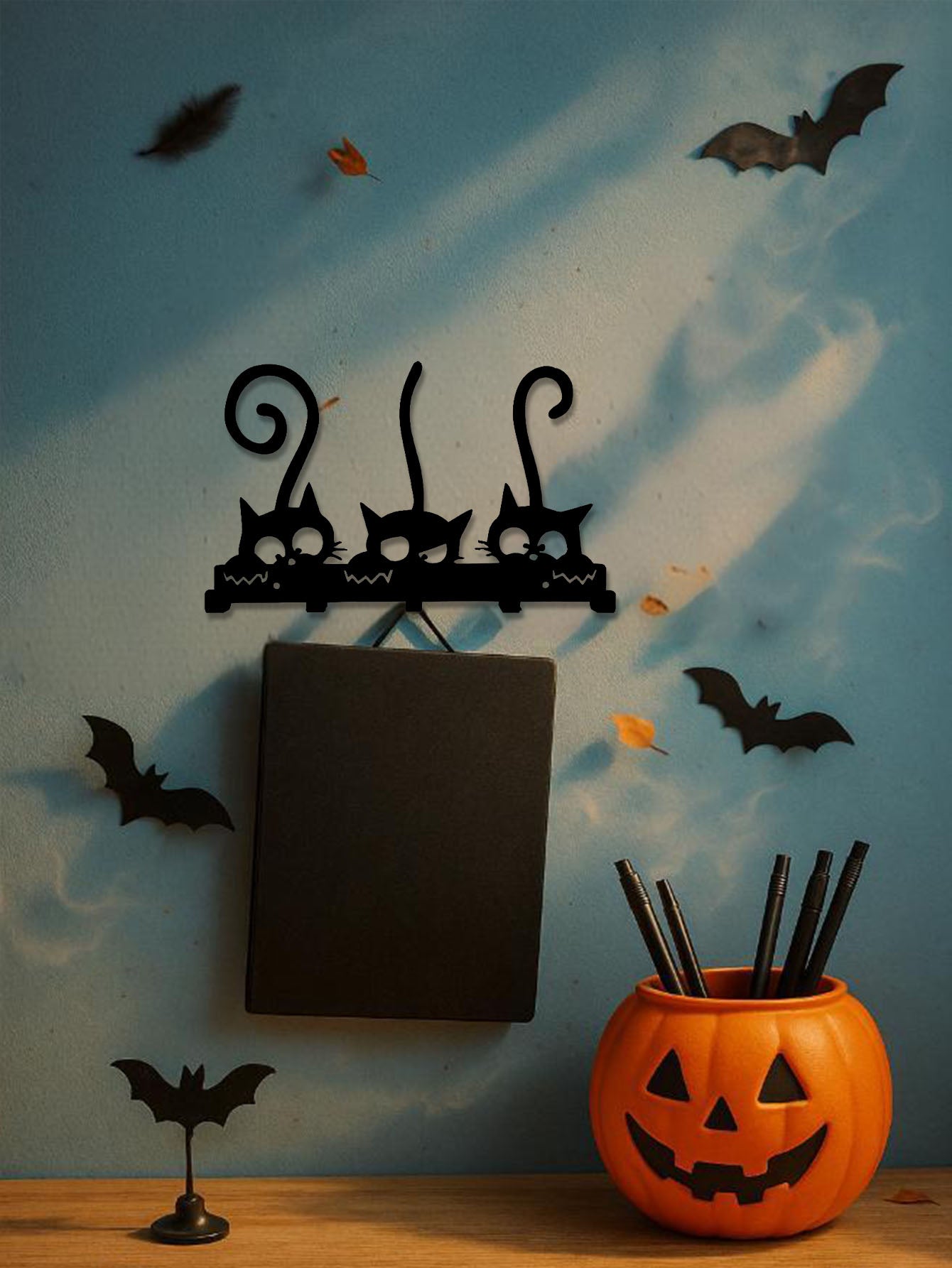 Black 5-hook cat design key and coat rack, orange jack-o'-lantern vase, and bats decor on a blue wall.